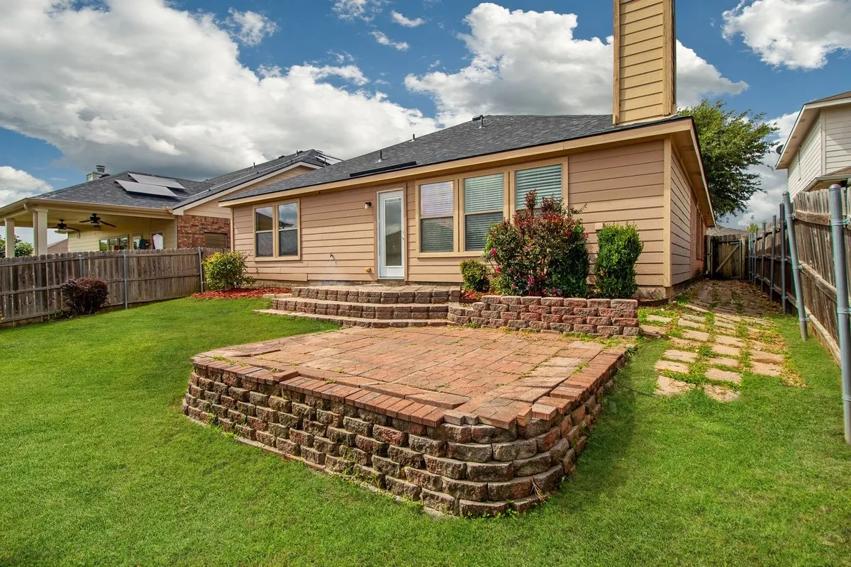 Expansive backyard featuring a tiered paver patio with a retaining wall, a manicured lawn, and a light-colored siding exterior