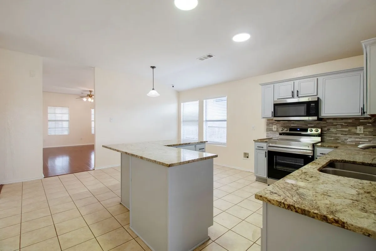 Kitchen featuring light cabinetry, stainless steel appliances, speckled stone countertops, and a tiled backsplash