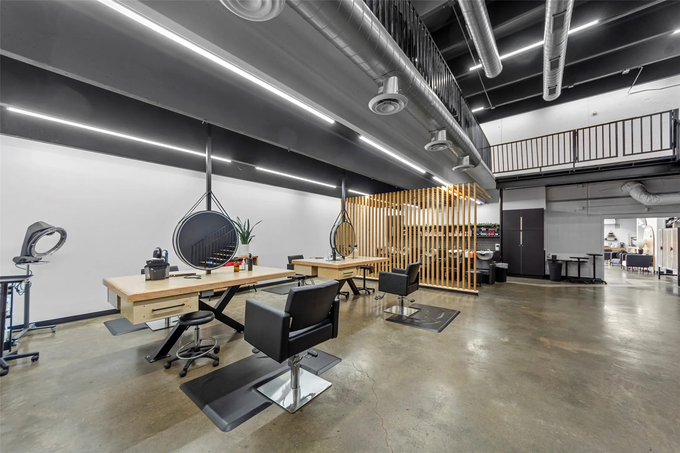Spacious commercial interior featuring concrete flooring, an exposed ceiling with ductwork, and a second-story mezzanine with metal railings