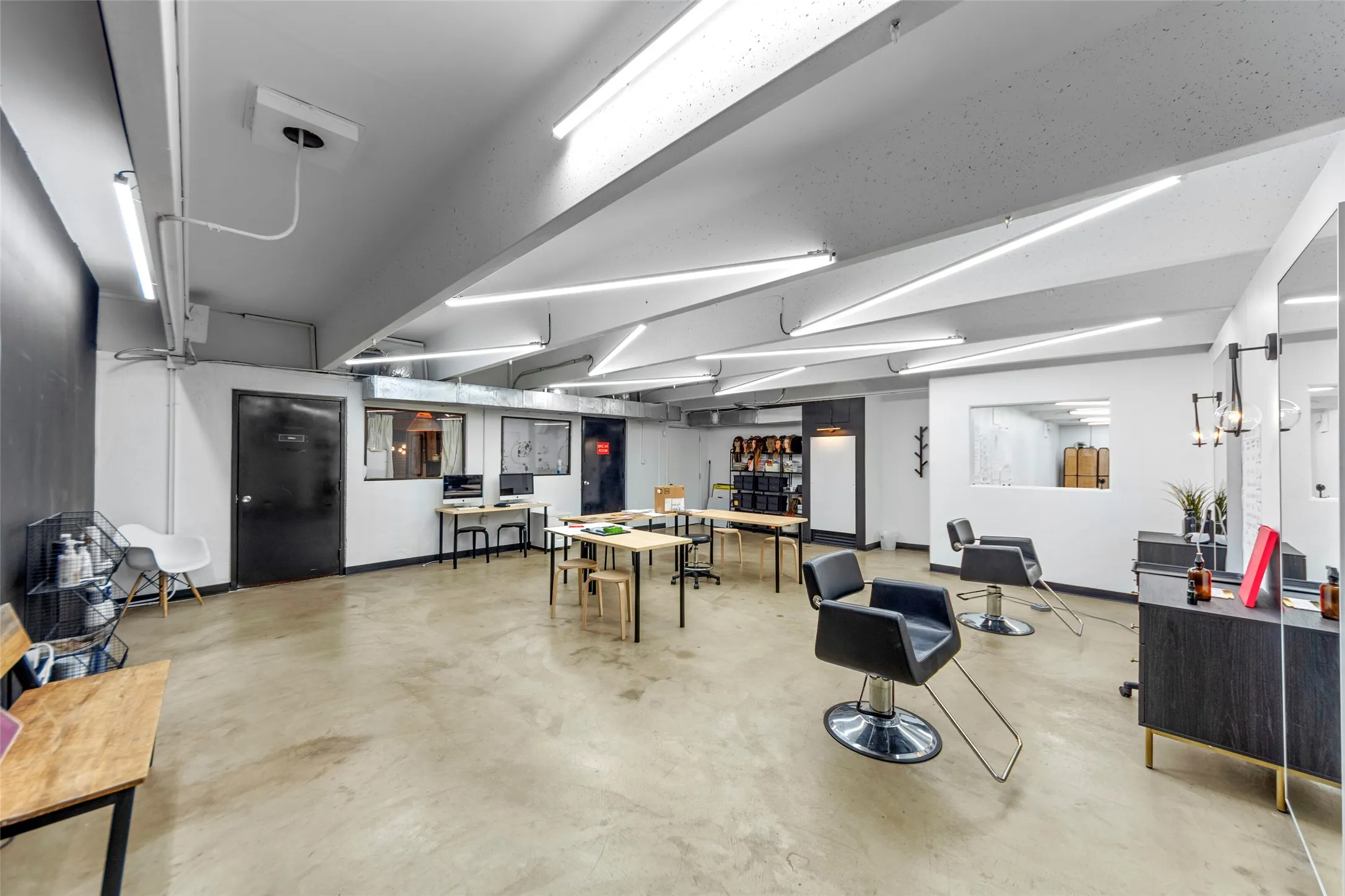 Spacious open-concept commercial interior featuring concrete flooring, modern linear lighting, exposed conduit, and a dark accent wall
