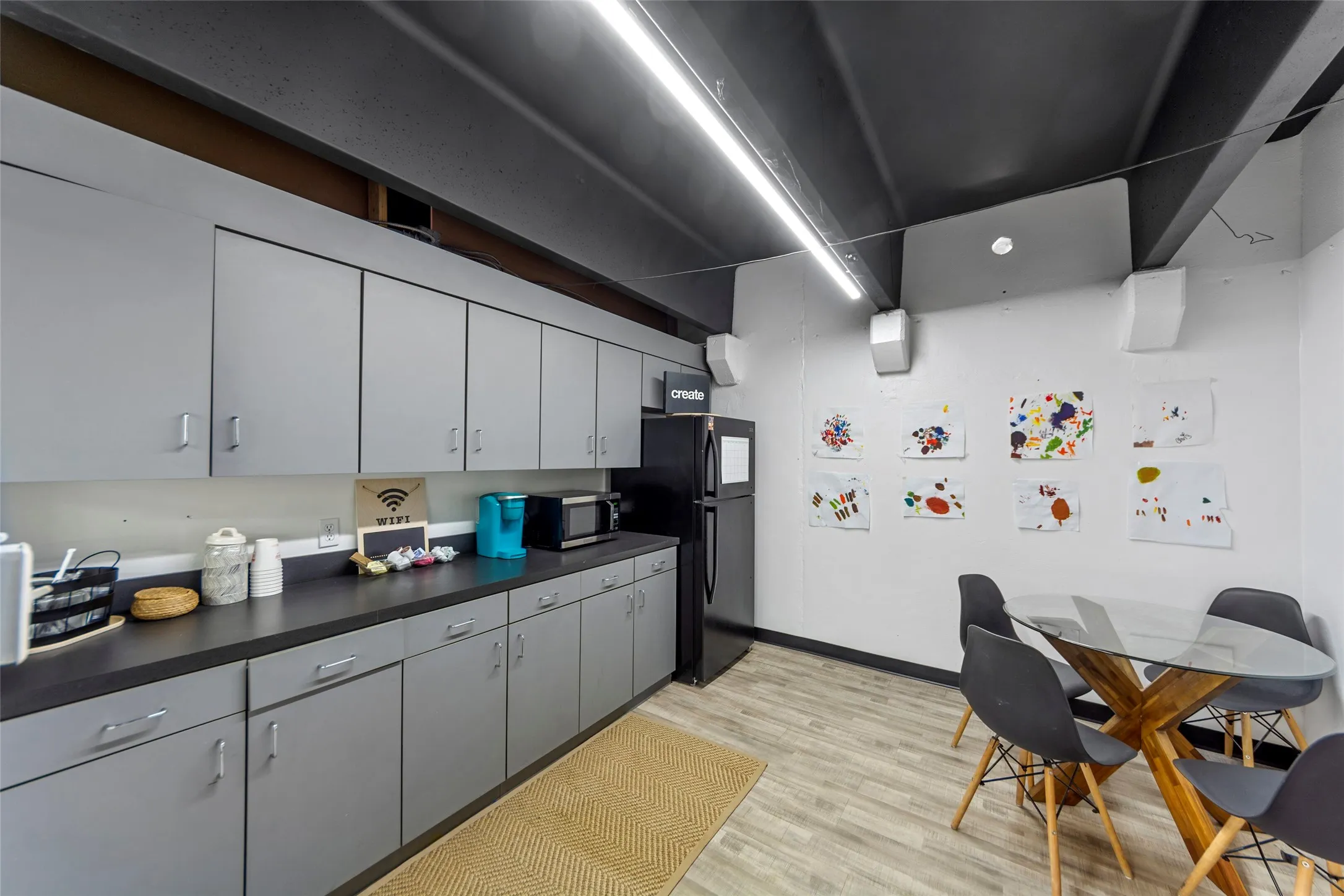 Contemporary kitchen with extensive grey cabinetry, dark countertops, and wood-finish flooring
