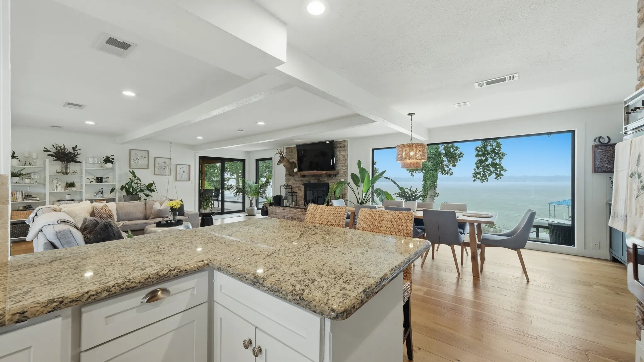 Spacious open-concept interior featuring light wood-finish flooring, recessed lighting, and a large picture window with extensive water scenery