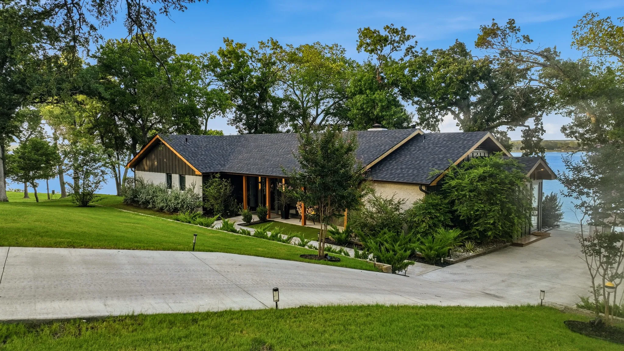 Waterfront residence featuring a stone and wood-finish exterior, a dark shingle roof, and a concrete driveway