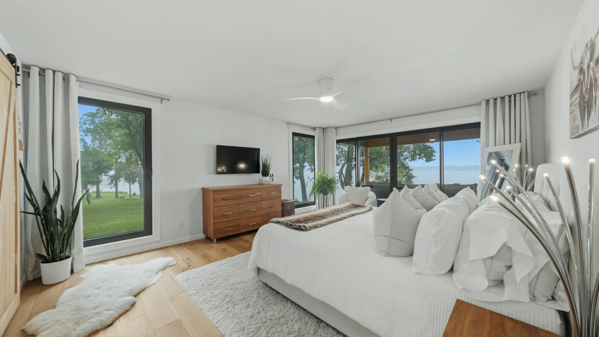 Spacious room featuring light wood-finish flooring, white walls, and multiple large windows showcasing a waterfront landscape