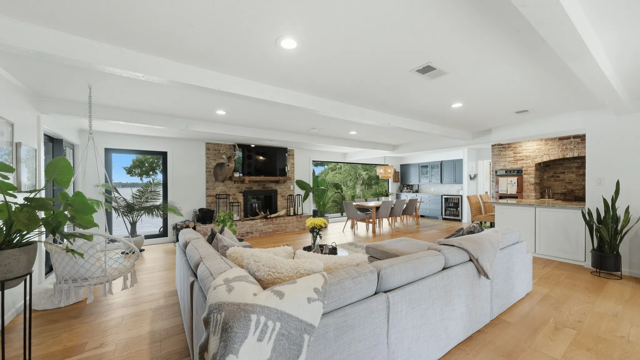 Open-concept living area featuring light wood-finish flooring, recessed lighting, and a stone-clad fireplace