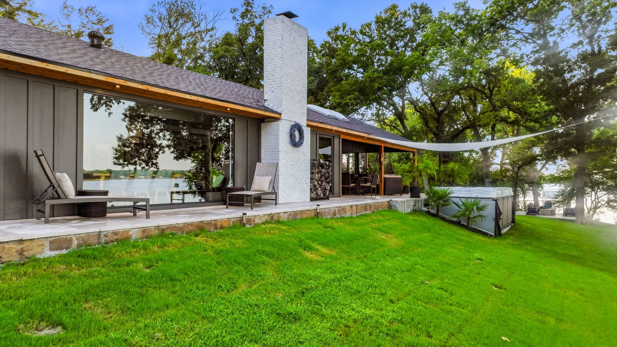 Expansive rear facade featuring a large picture window, a stone patio, and a covered outdoor living area