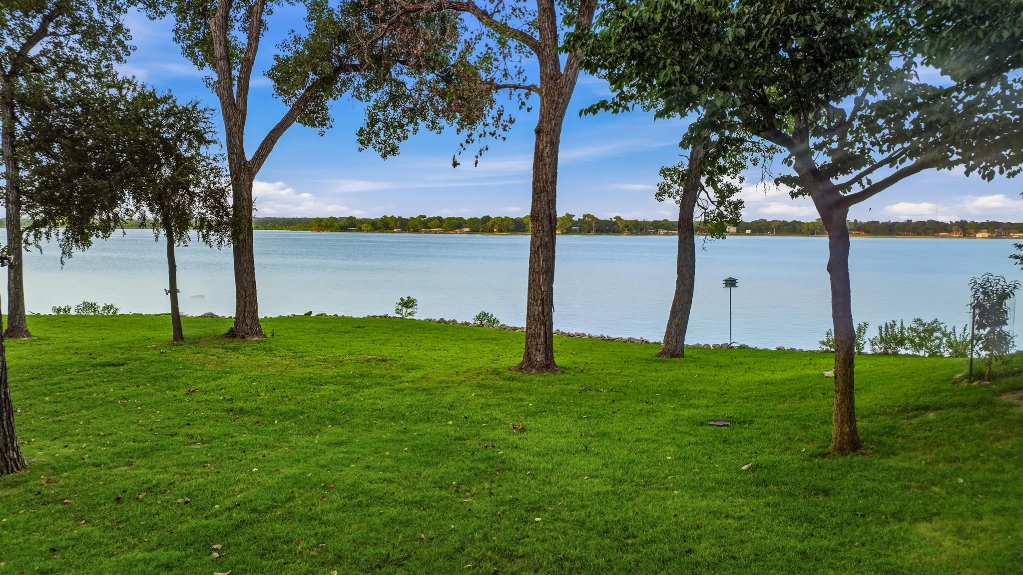 Expansive waterfront property featuring a manicured lawn, mature trees, and direct access to the lake