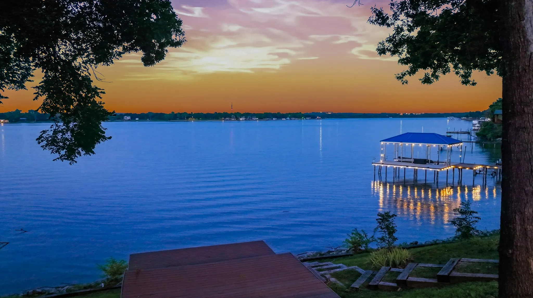 Expansive waterfront with a covered boat dock, multi-level decking, and stone-edged landscaping