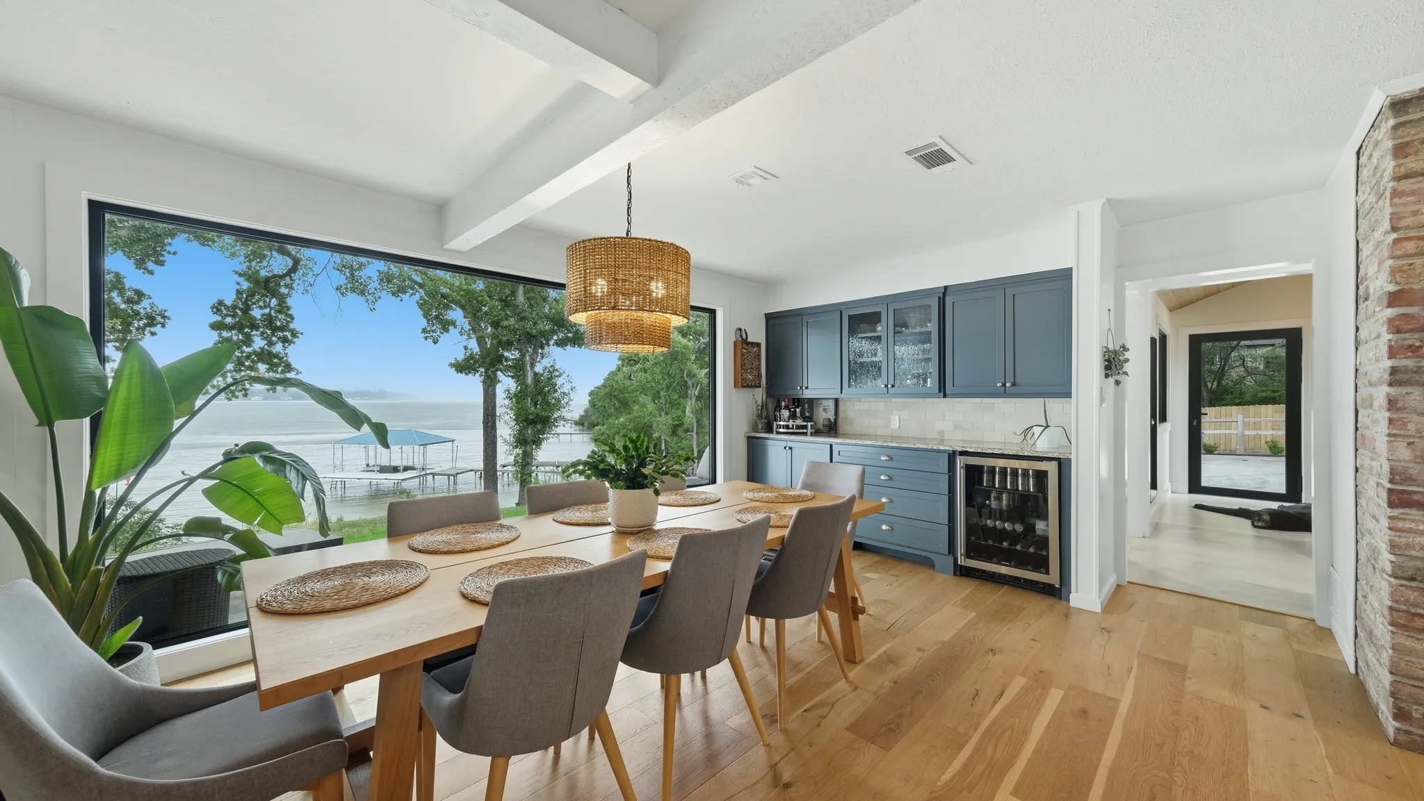 Dining area featuring expansive waterfront window, wood-finish flooring, exposed ceiling beams, and a built-in beverage center with a wine refrigerator