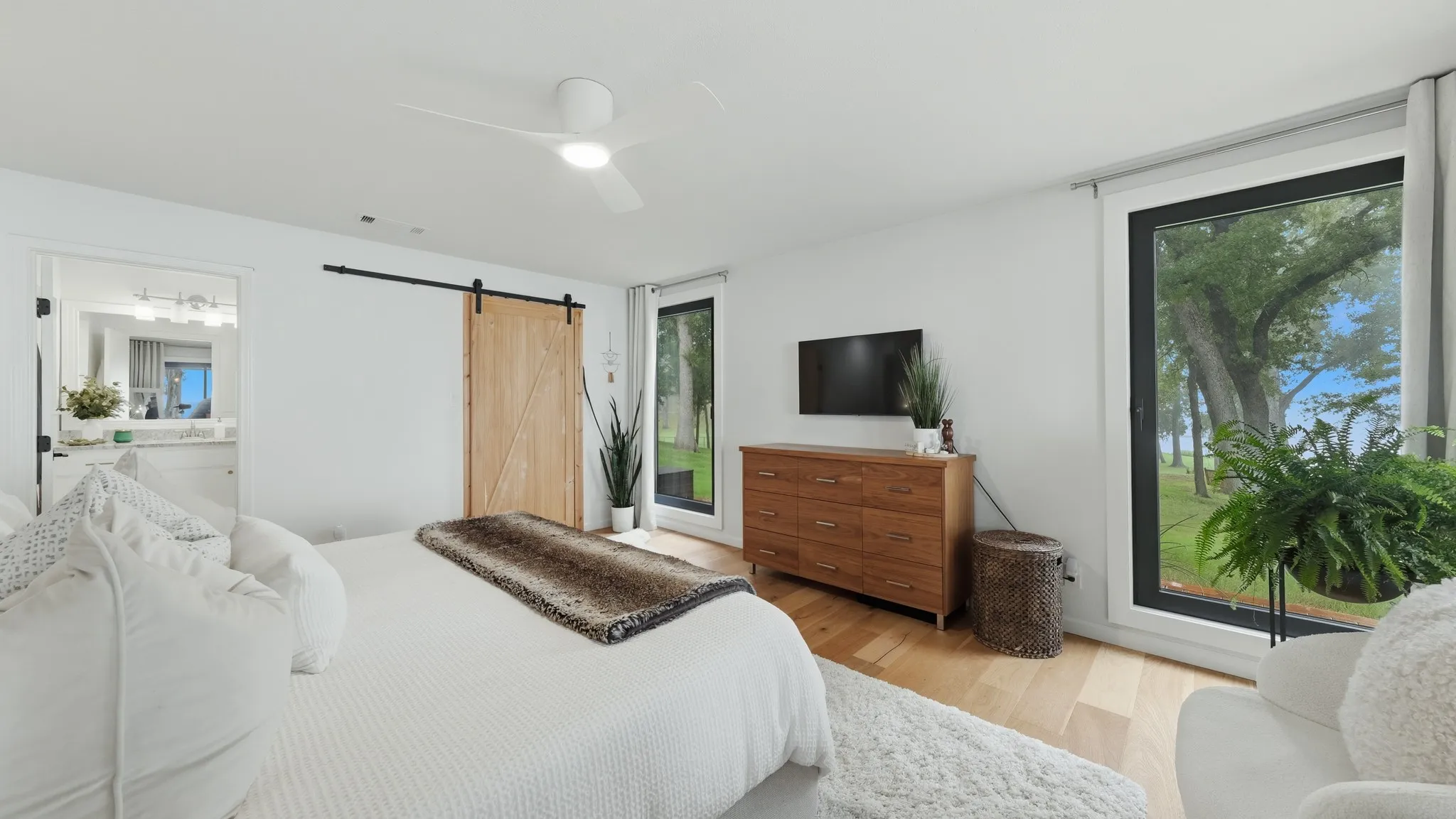 Bright interior space featuring wood-finish flooring, a contemporary ceiling fan, and large windows with outdoor views