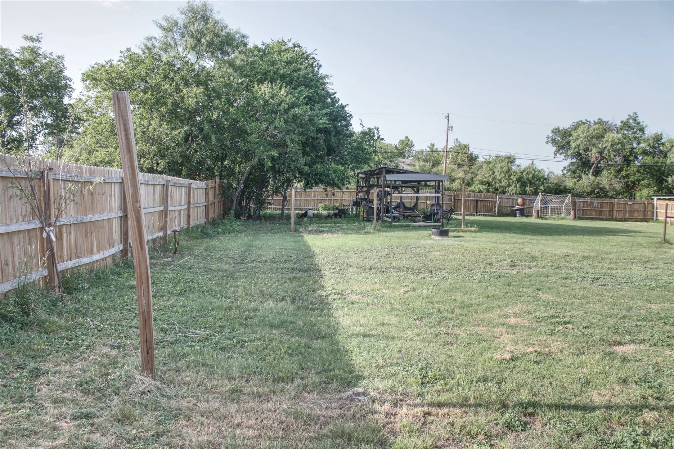 Spacious fenced yard featuring a wood privacy fence, mature trees, and a shaded outdoor structure