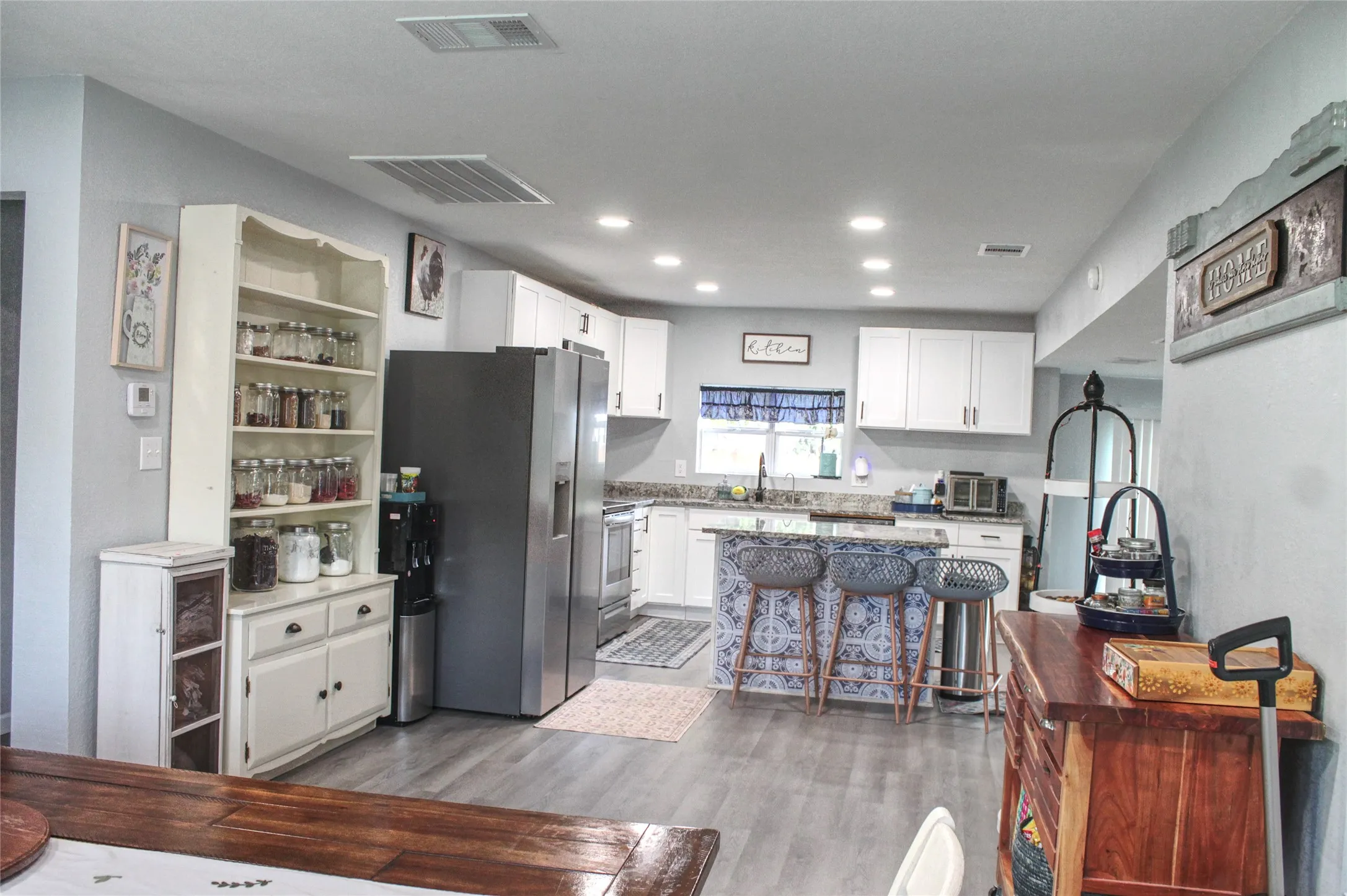 Modern kitchen featuring white cabinetry, grey wood-finish flooring, a patterned kitchen island, granite countertops, and stainless steel appliances