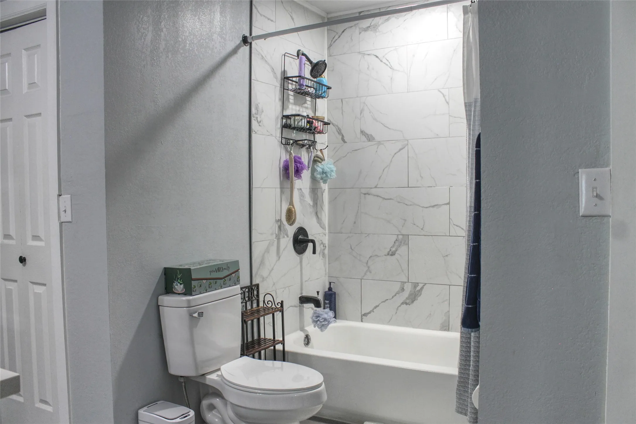 Bathroom featuring a white bathtub with a black shower fixture, white subway tile surround with gray veining, and a white toilet