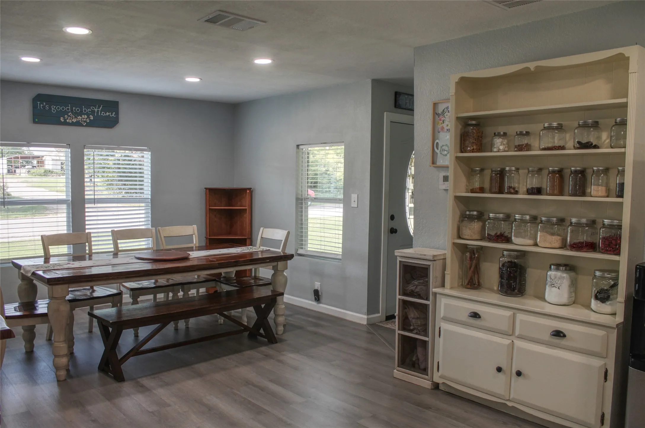 Spacious room featuring multiple windows with blinds, recessed lighting, wood-finish flooring, light gray walls, and a built-in display hutch with cabinetry