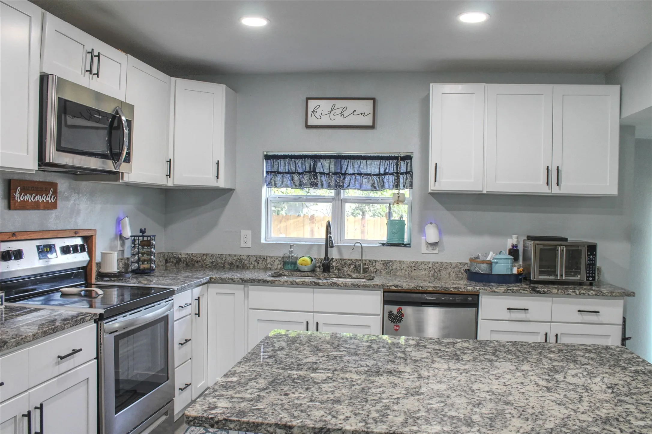 Kitchen featuring white shaker-style cabinetry, stainless steel appliances, speckled stone countertops, and recessed lighting