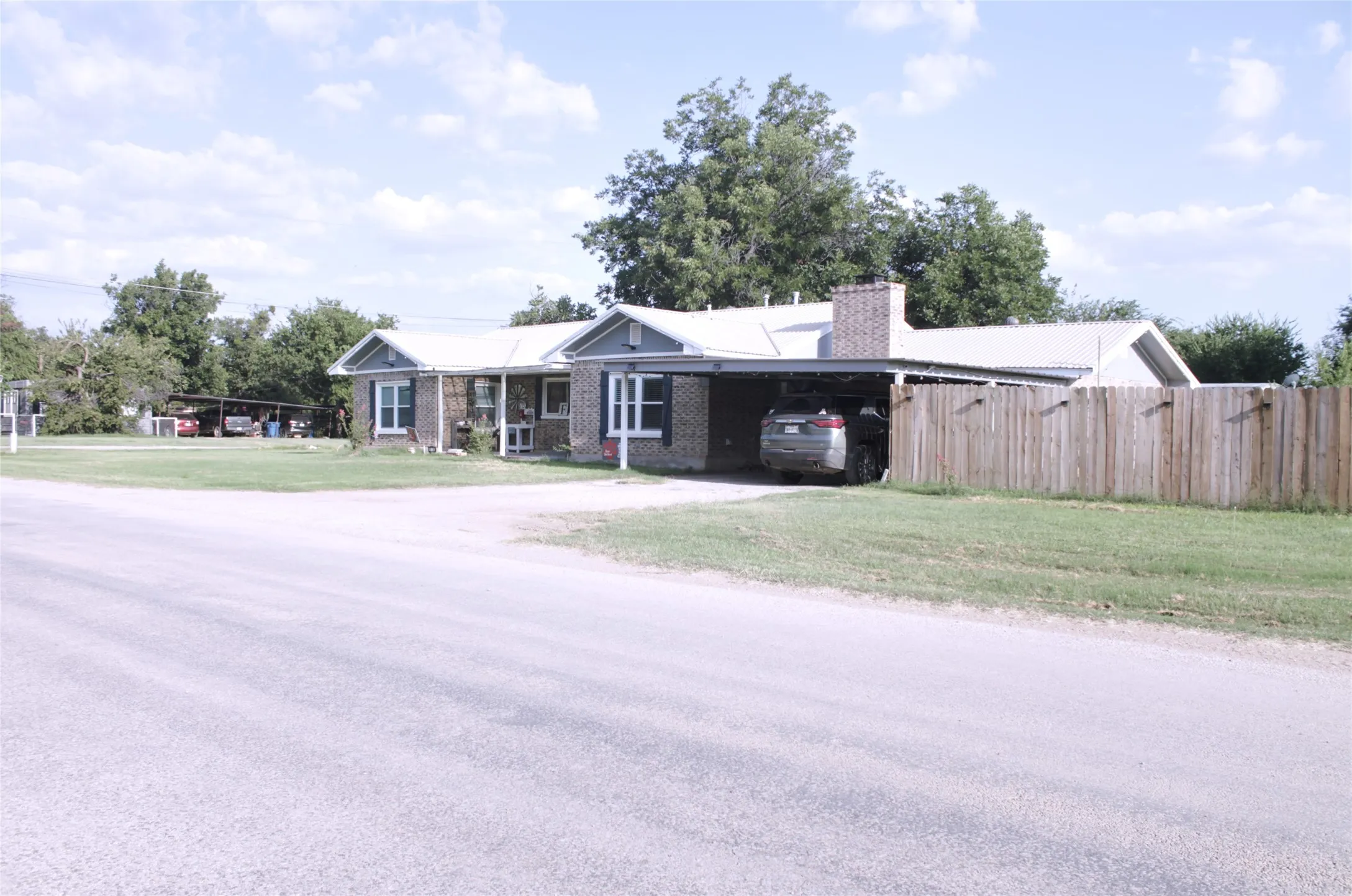 Brick exterior with white trim, covered carport, white gable roof, and a wood fence
