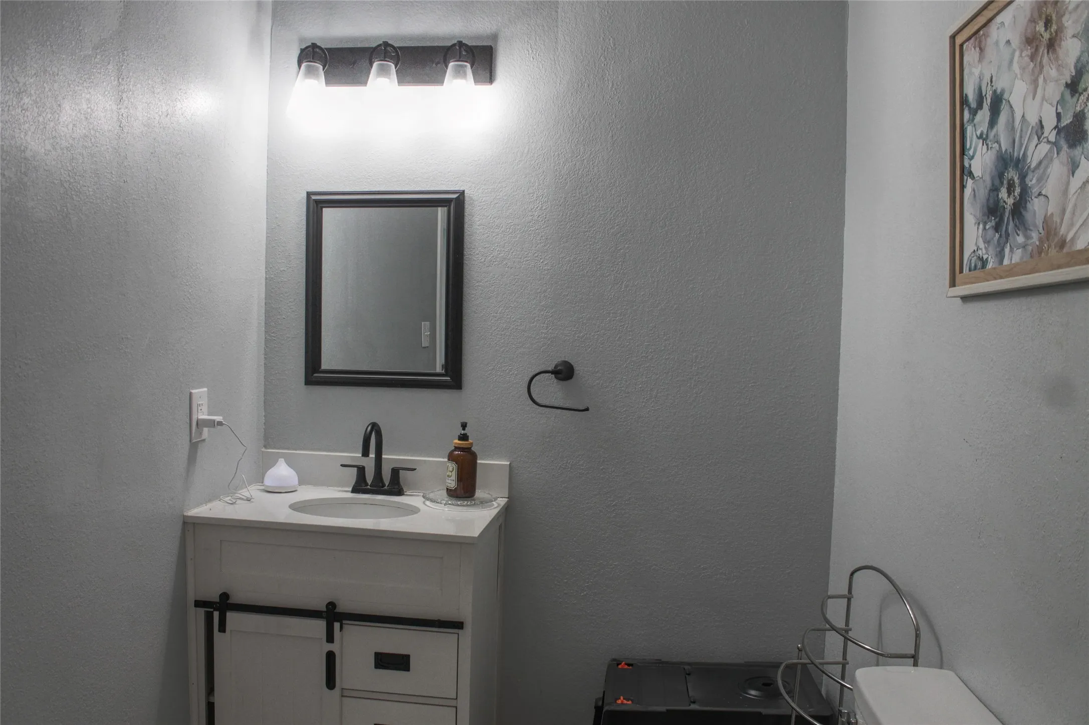 Vanity with slide-out door, integrated sink, black-finish faucet, framed mirror, and wall-mounted light fixture