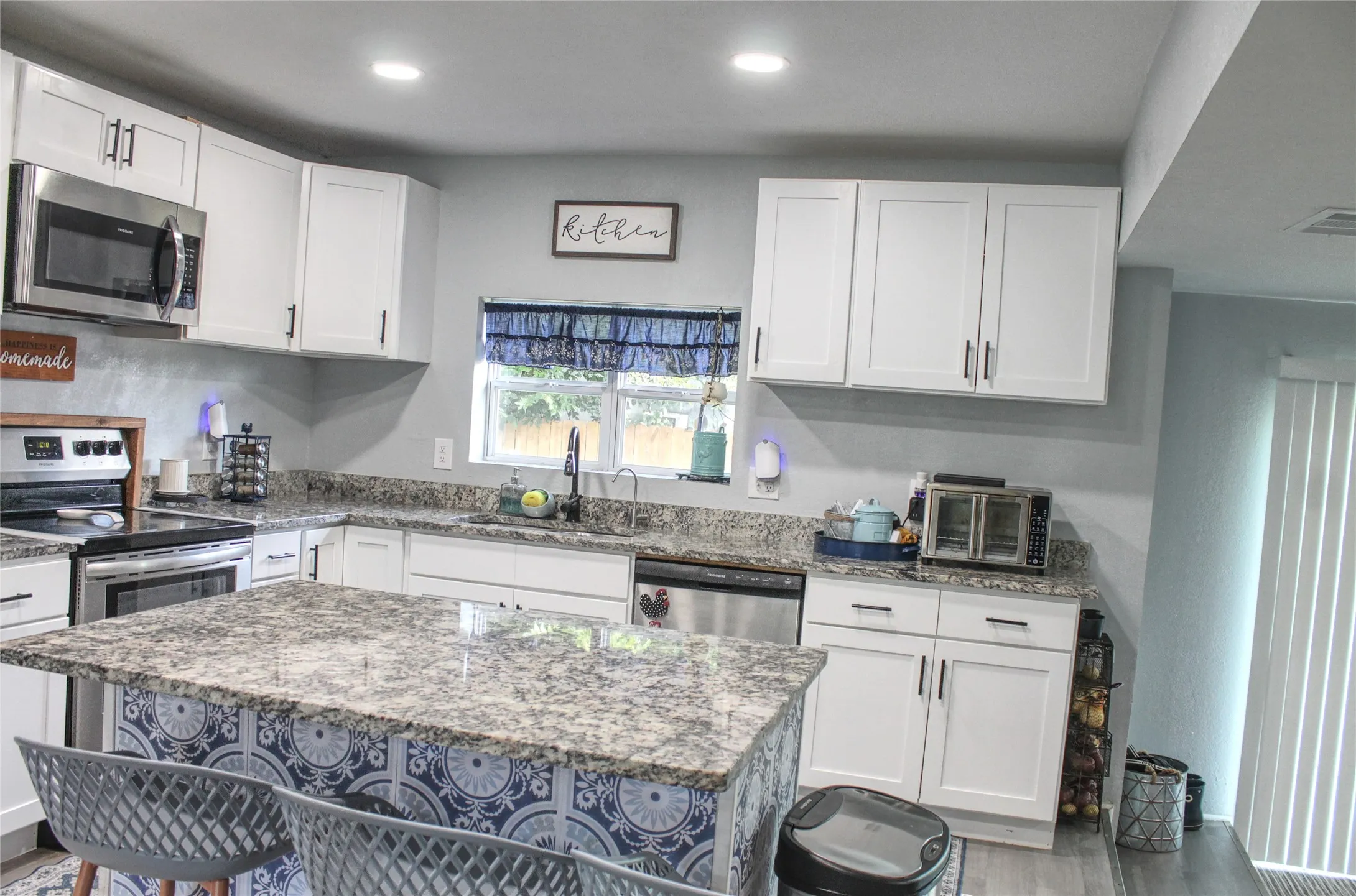 Modern kitchen featuring white cabinetry with dark hardware, stainless steel appliances, and a central island with a patterned facade