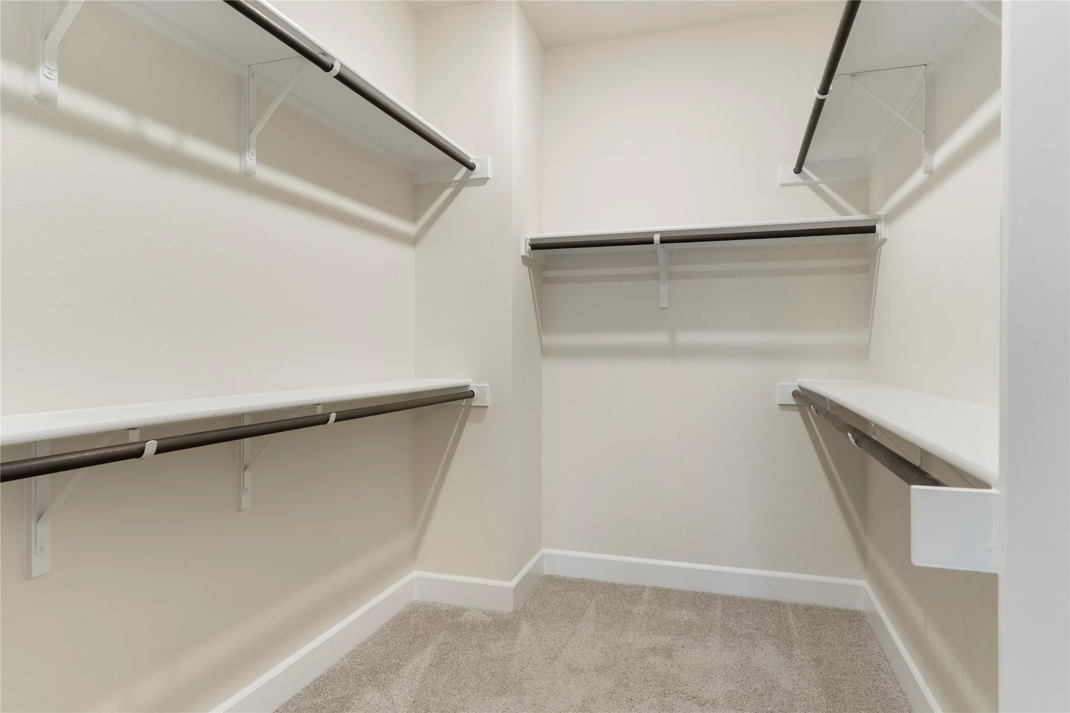Built-in shelving and hanging rods, neutral-toned carpeting, and white baseboards