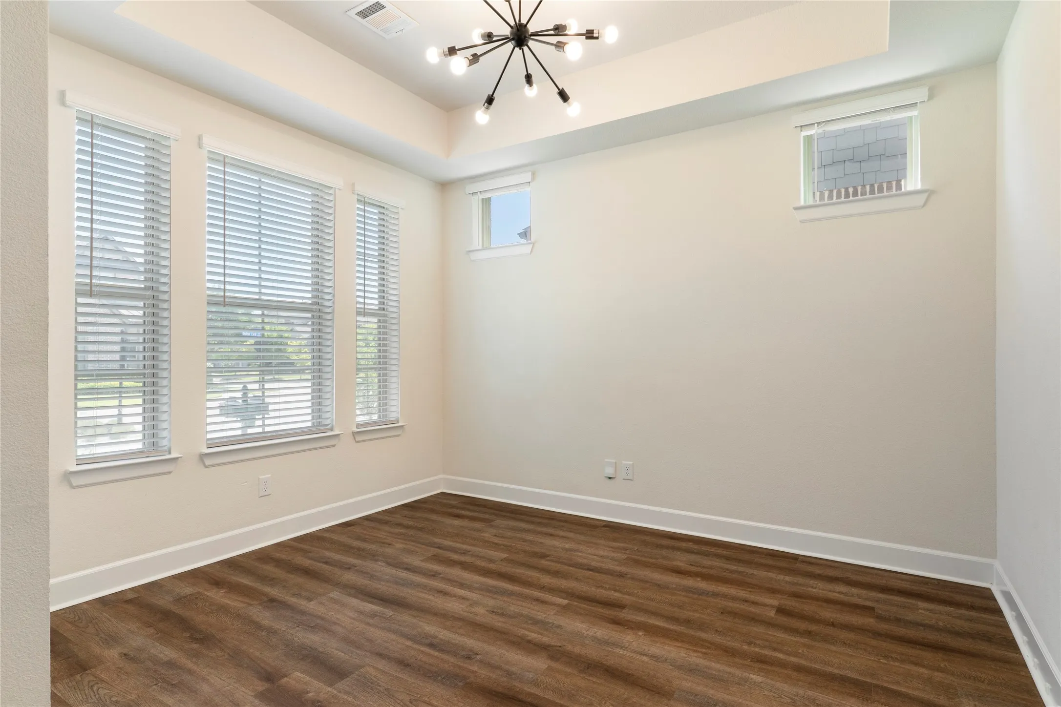 Wood-finish flooring with white baseboards, a modern sputnik chandelier, and a tray ceiling