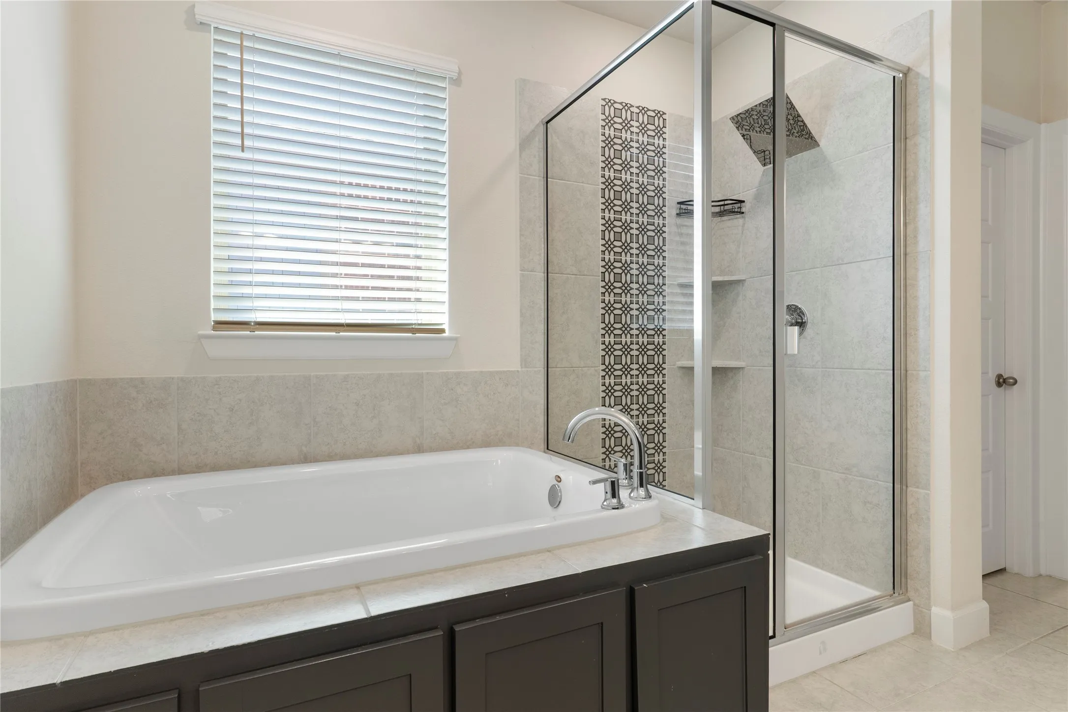 Soaking tub with deck-mounted faucet, separate glass-enclosed shower with tiled surround and decorative accent, built-in shower niches, and an overhead rain shower