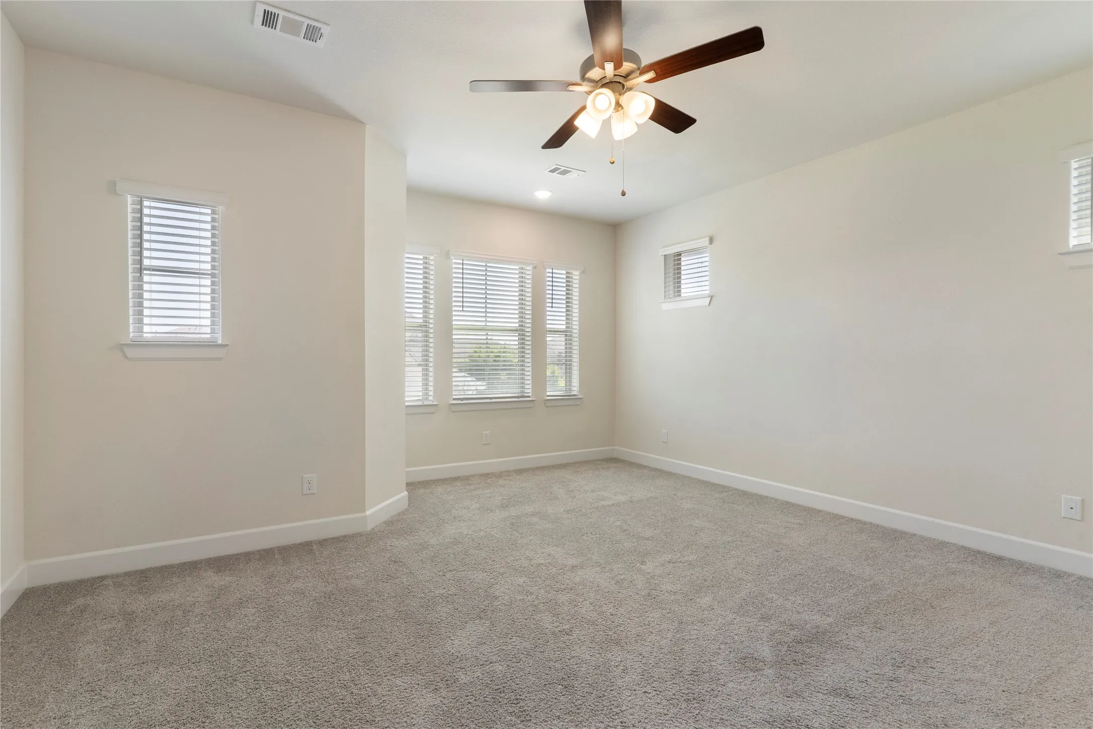 Spacious room featuring neutral carpeting, multiple windows with blinds, a ceiling fan with integrated lighting, and recessed lighting