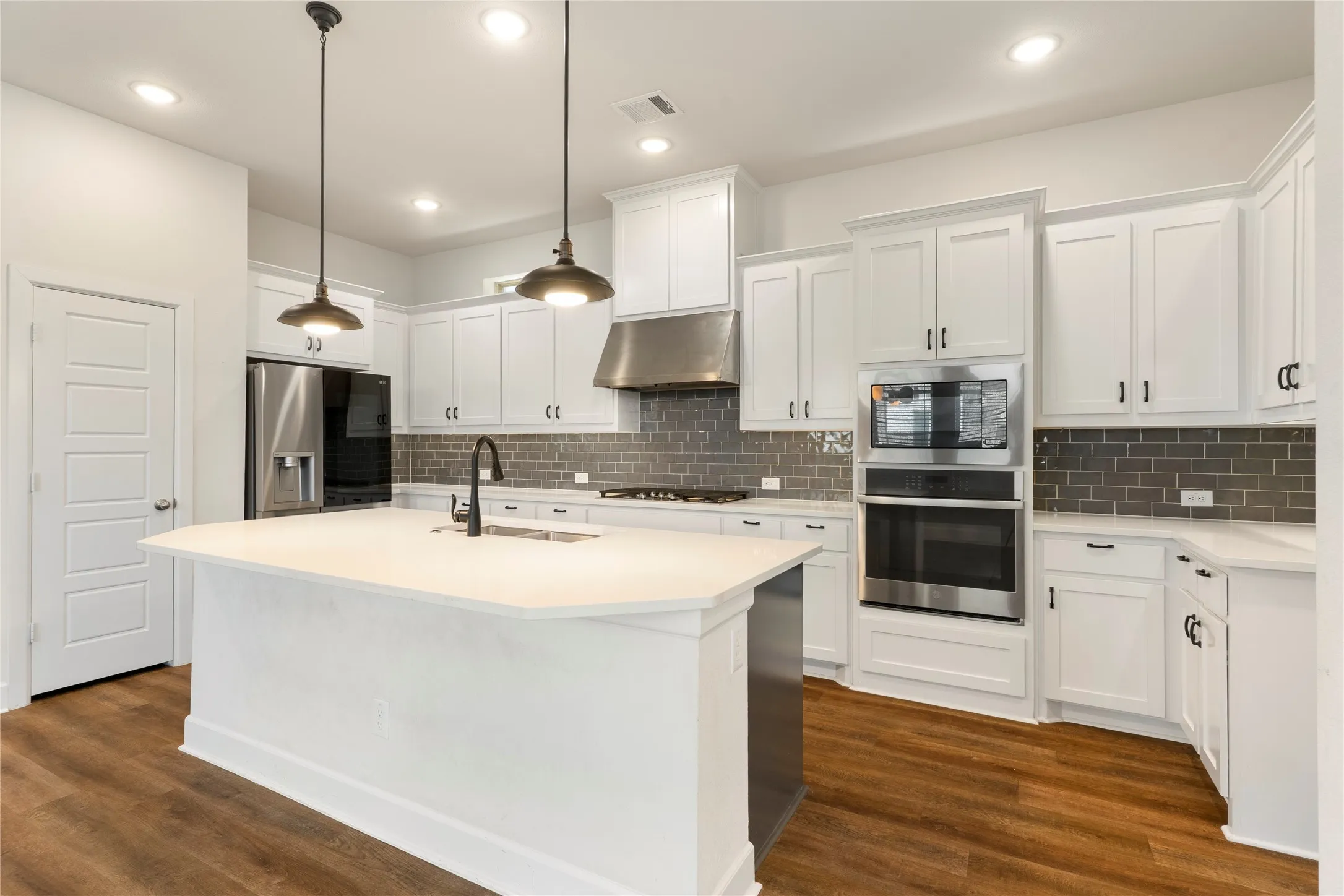 White shaker cabinetry, stainless steel appliances, kitchen island with sink, wood-finish flooring, and recessed lighting