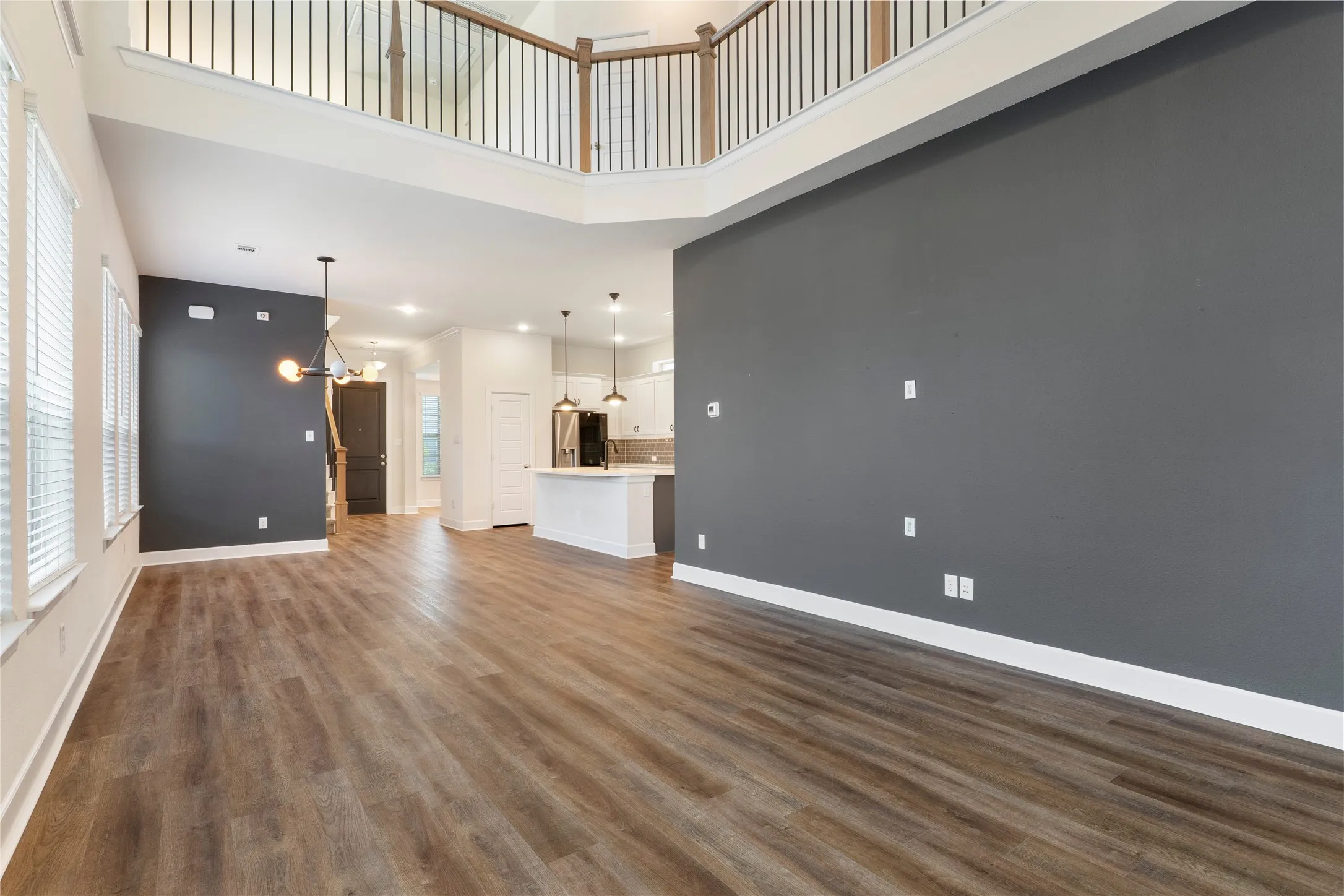 Two-story living area with wood-finish flooring, abundant natural light, and modern lighting fixtures