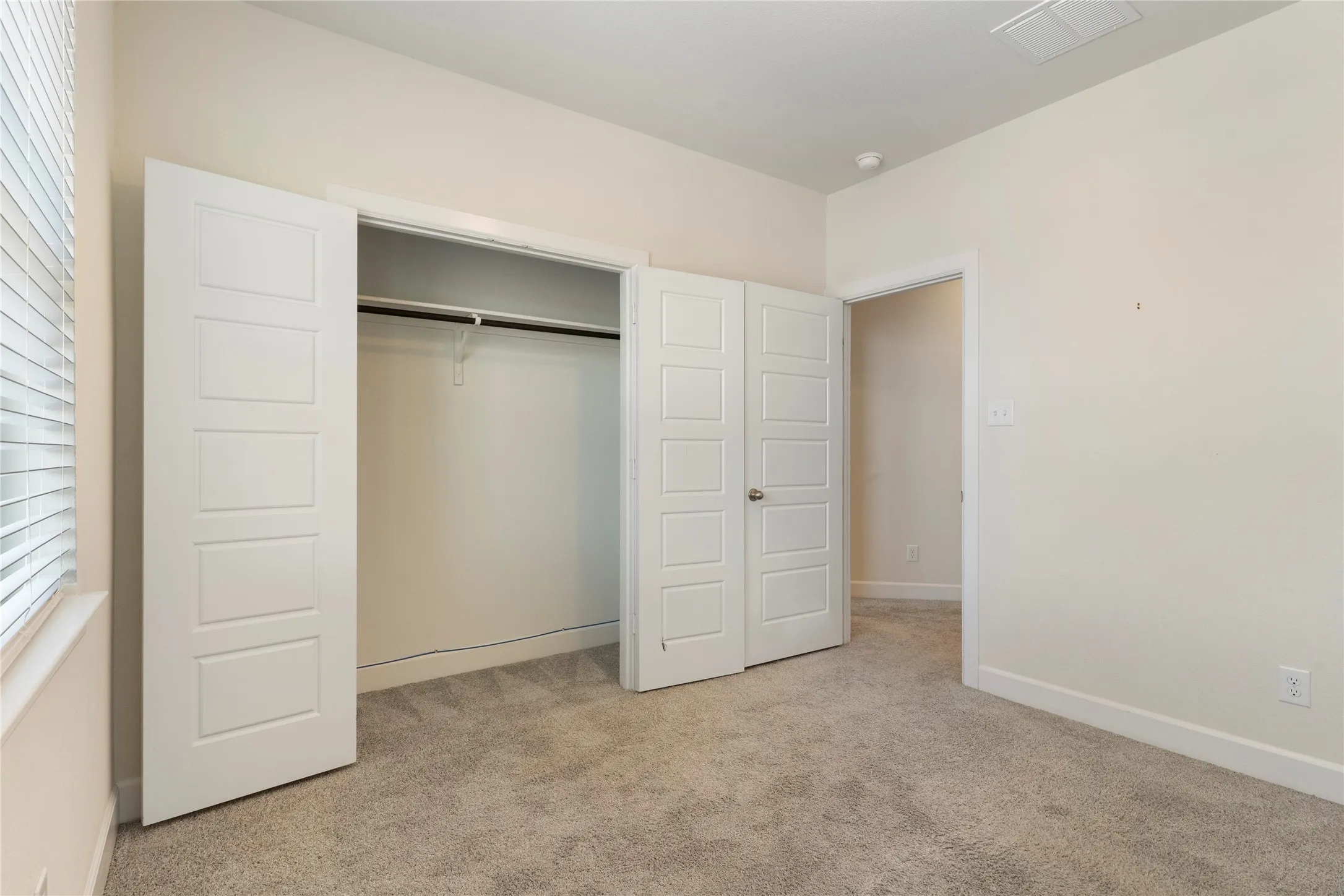 Carpeted room with a double-door closet featuring panel doors, a single clothes rod, and a window with horizontal blinds