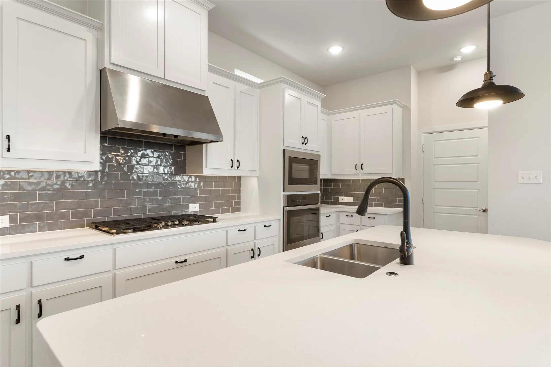 White cabinetry, stainless steel appliances, dual basin sink, subway tile backsplash, and a central island with a solid surface countertop