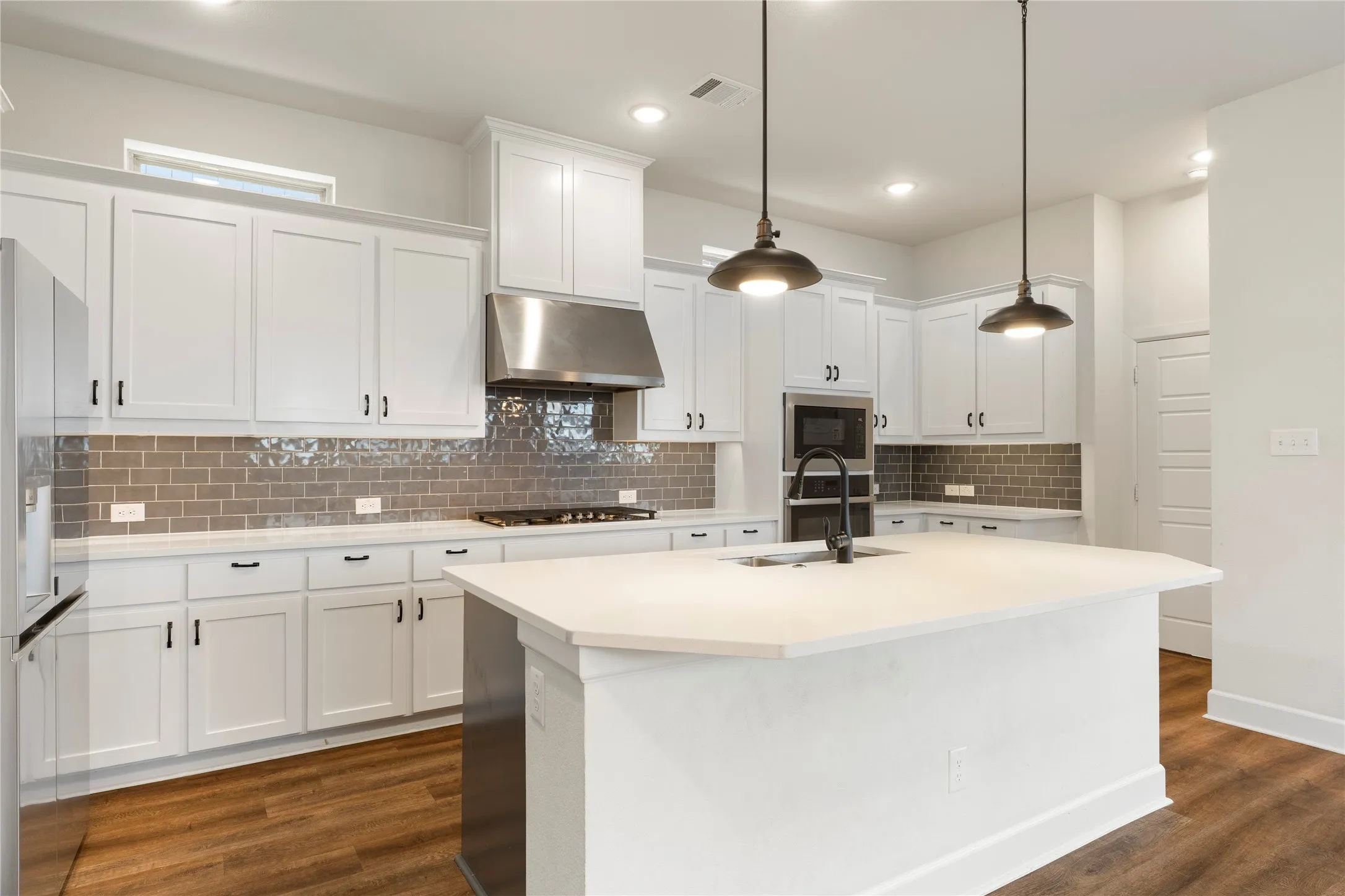 White cabinetry with black hardware, tile backsplash, stainless steel appliances, large kitchen island with integrated sink, and wood-finish flooring