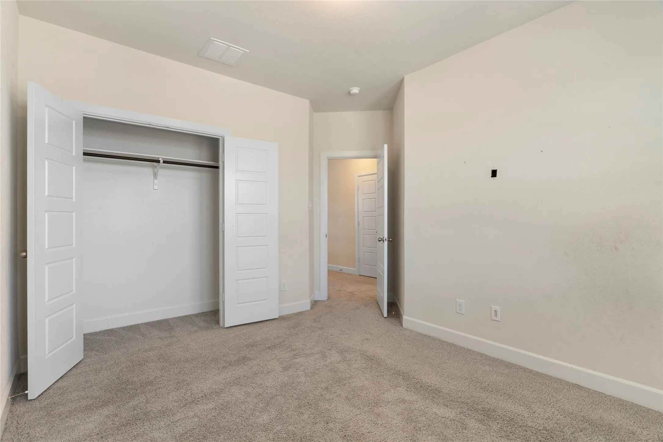 Neutral tone wall paint, light gray carpet, and an open closet with bi-fold panel doors