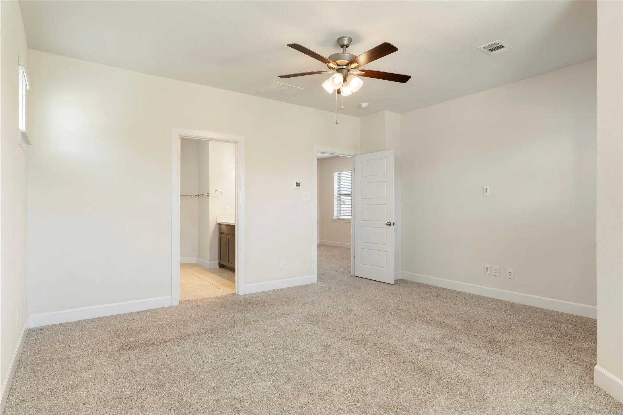 Neutral tone walls, light-colored carpeting, and a ceiling fan with integrated lighting