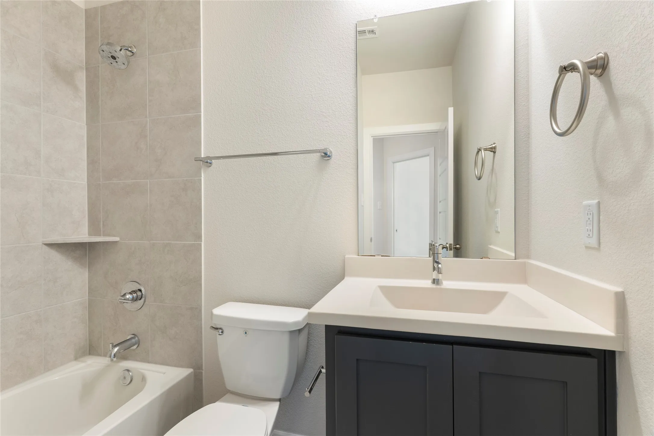 Bathroom featuring a white tub, light-toned wall tiling, dark gray vanity with white countertop, and a vanity mirror