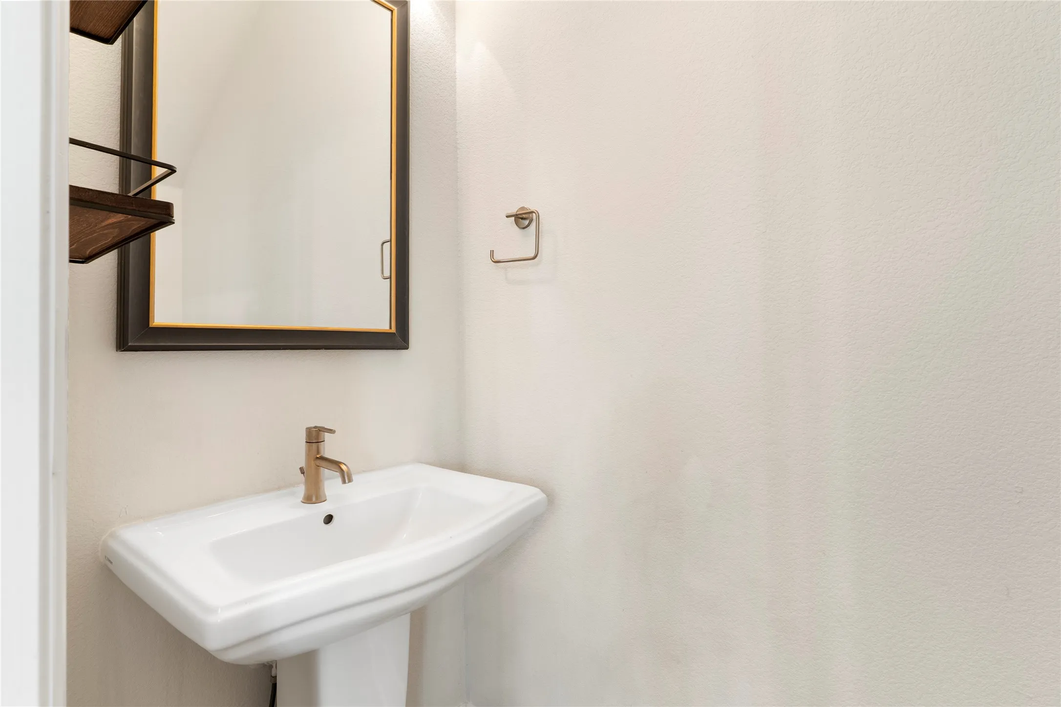 Pedestal sink with brass-finish faucet, framed mirror, and wall-mounted shelving