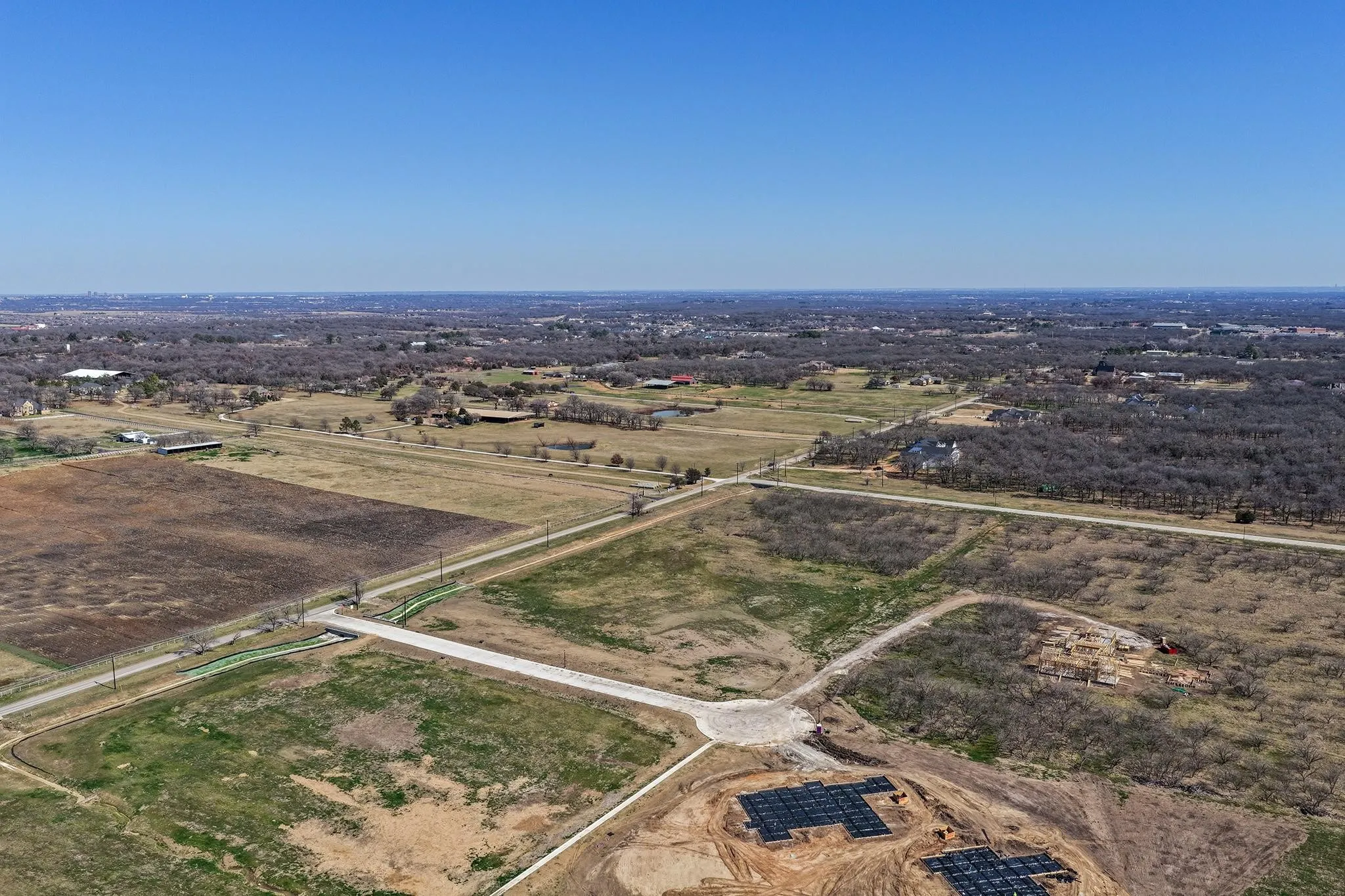 Expansive undeveloped land featuring a clear blue sky, numerous mature trees, and visible road infrastructure