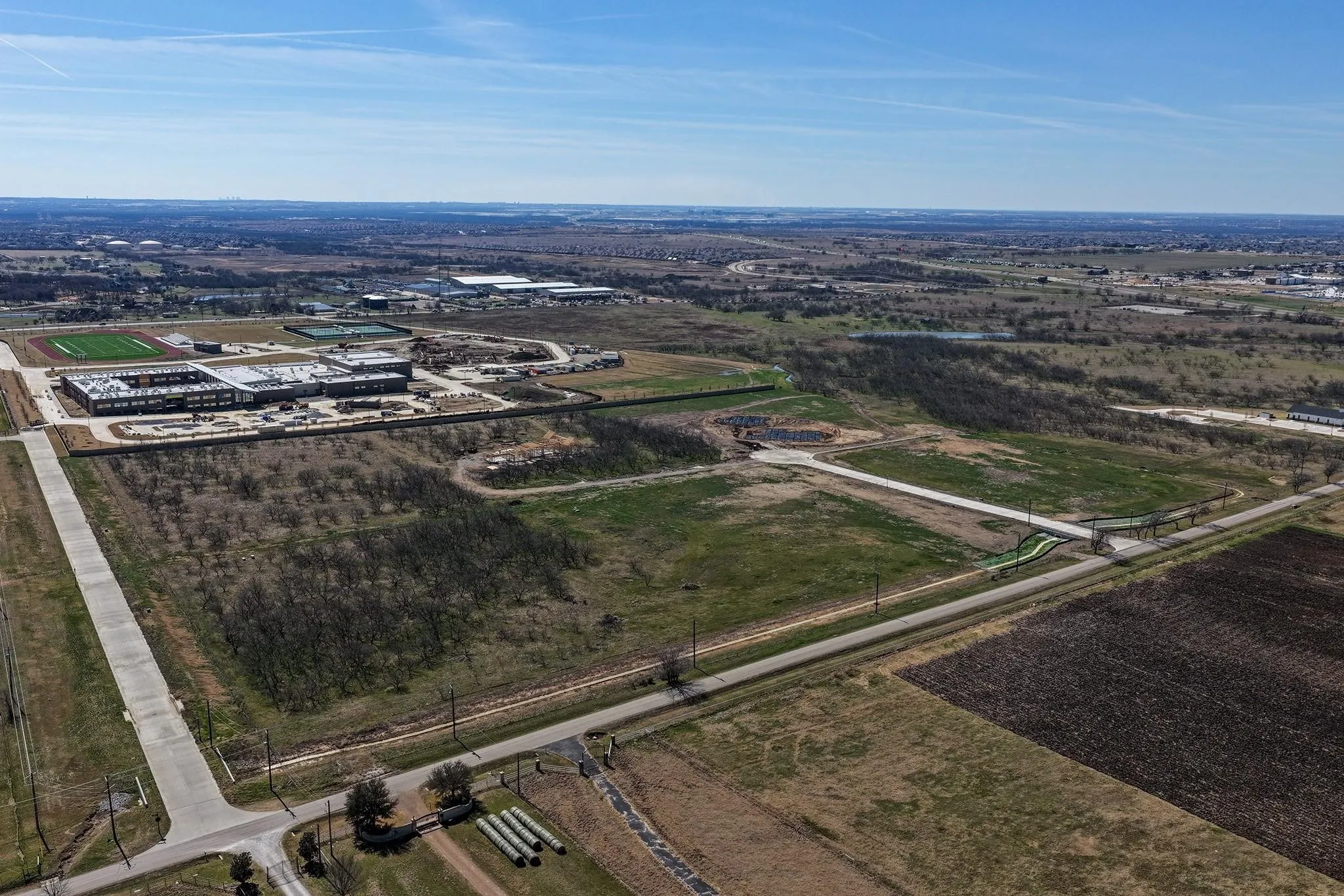 Aerial perspective of a developing area featuring a large institutional building under construction with multiple sports fields