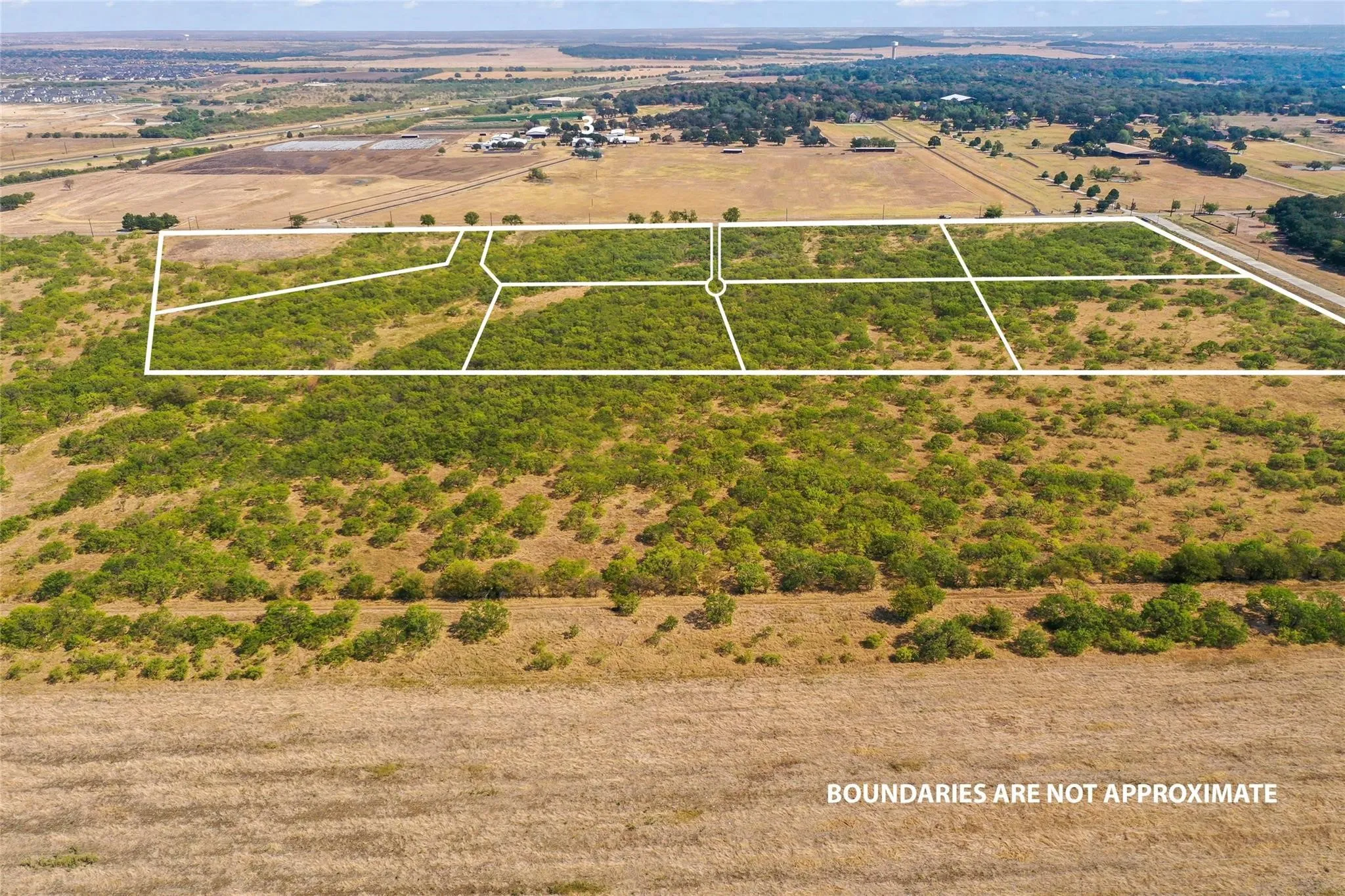 Expansive undeveloped land featuring multiple subdivided parcels, dense natural vegetation, and surrounding open fields