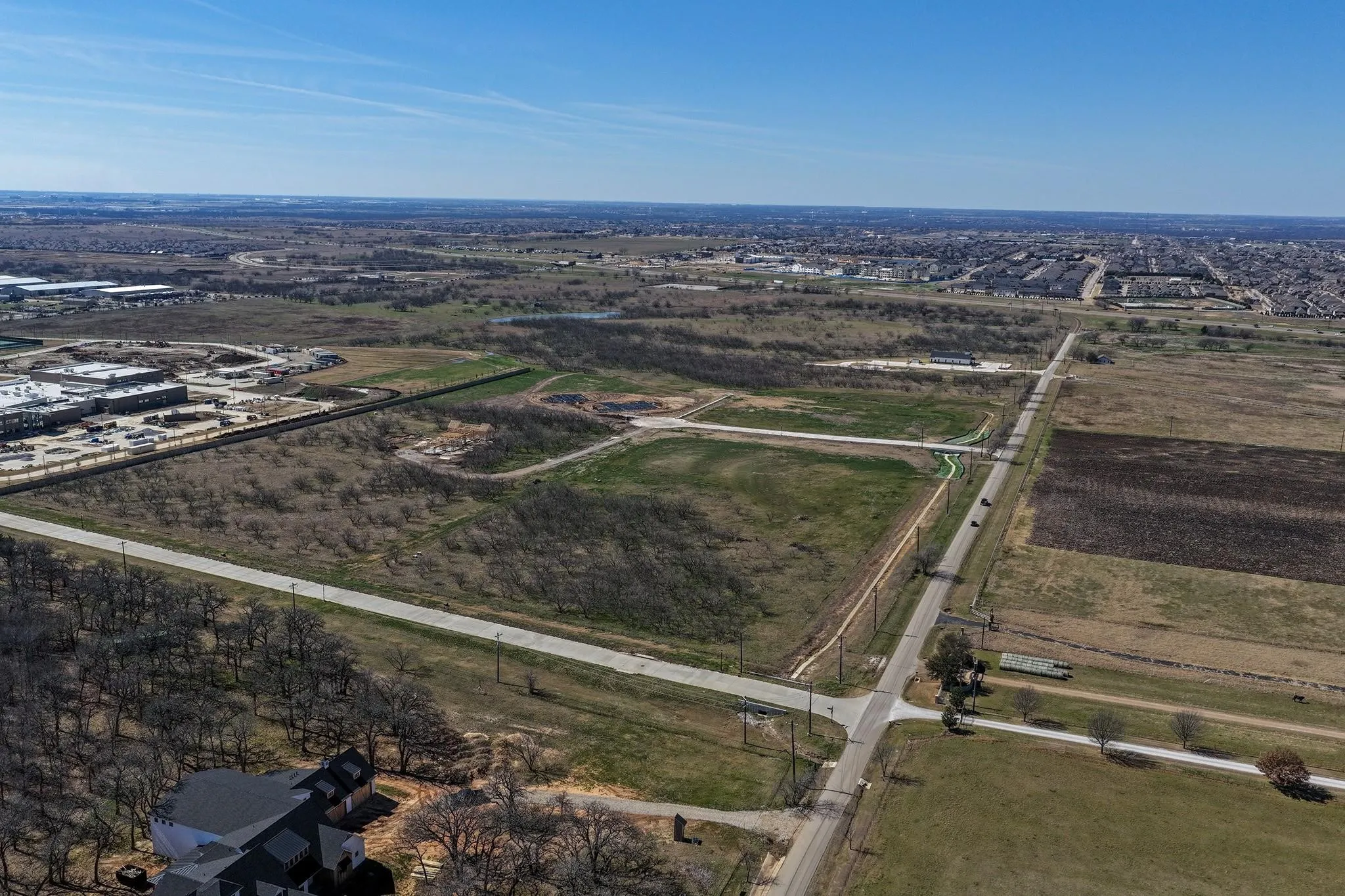 Expansive undeveloped land with visible road frontage, adjacent to existing commercial structures and residential developments