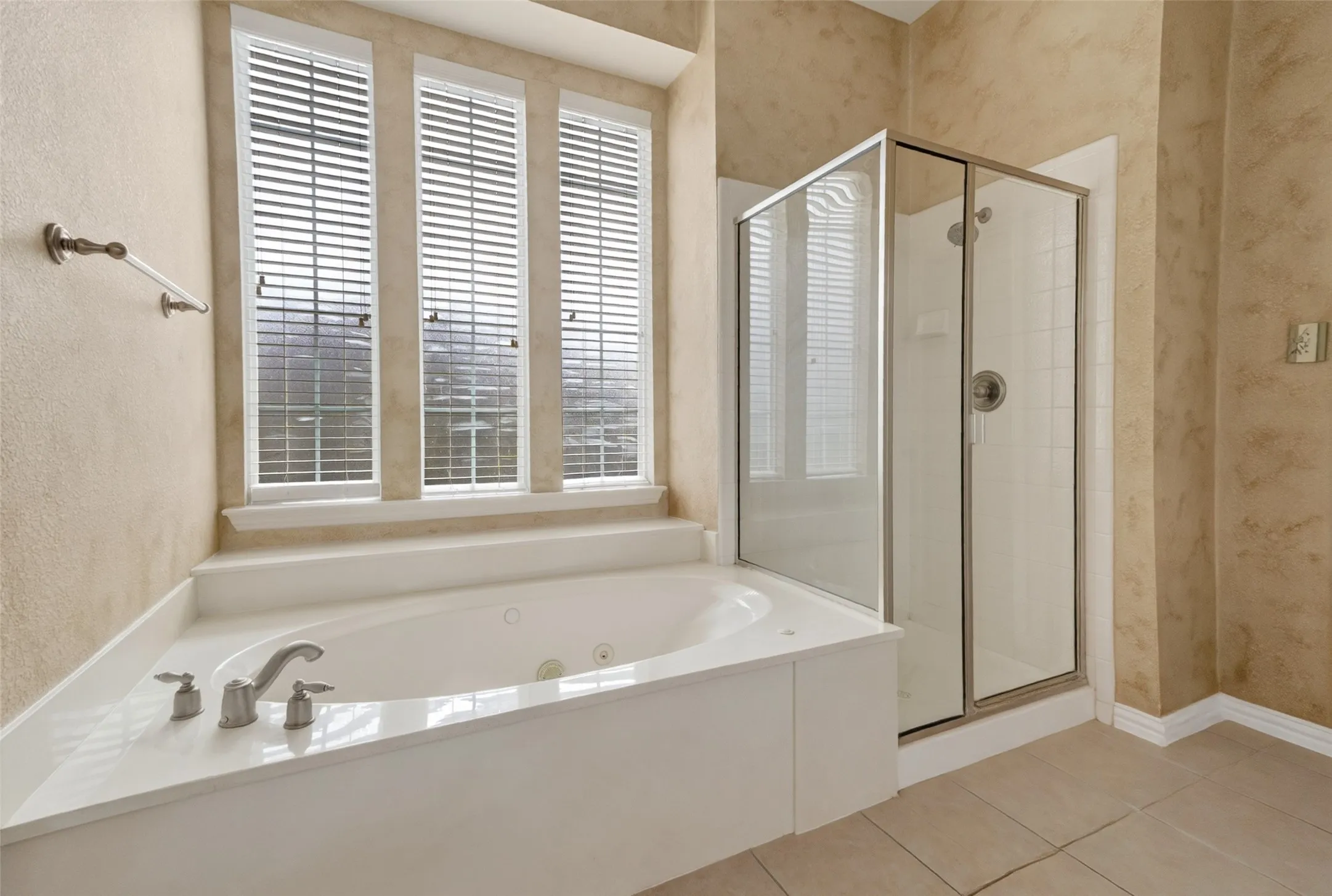 Soaking tub with deck-mounted brushed nickel fixtures, accompanied by three vertical windows with blinds