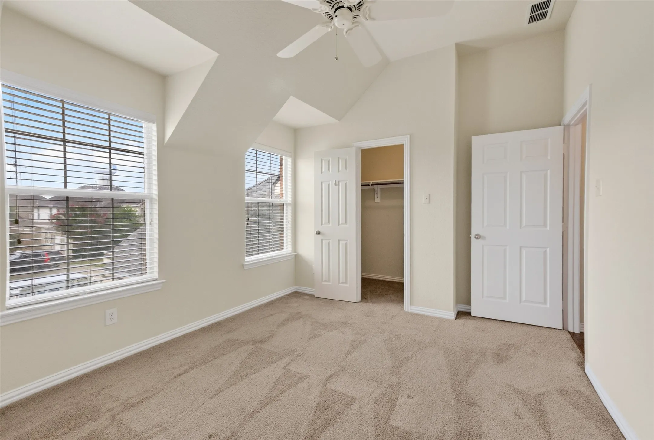 Carpeted room featuring multiple windows with blinds, a ceiling fan, and two paneled doors providing access