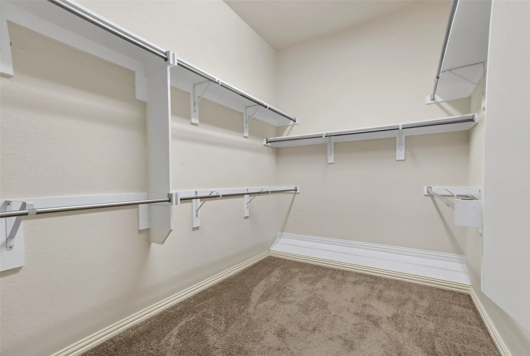Walk-in closet featuring built-in shelving, multiple hanging rods, light-toned carpeting, and a neutral wall finish