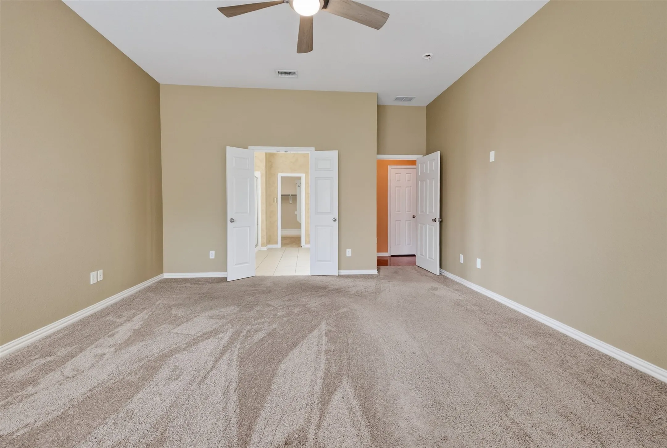 Spacious room featuring neutral carpeting, light beige walls, and a ceiling fan with light fixture