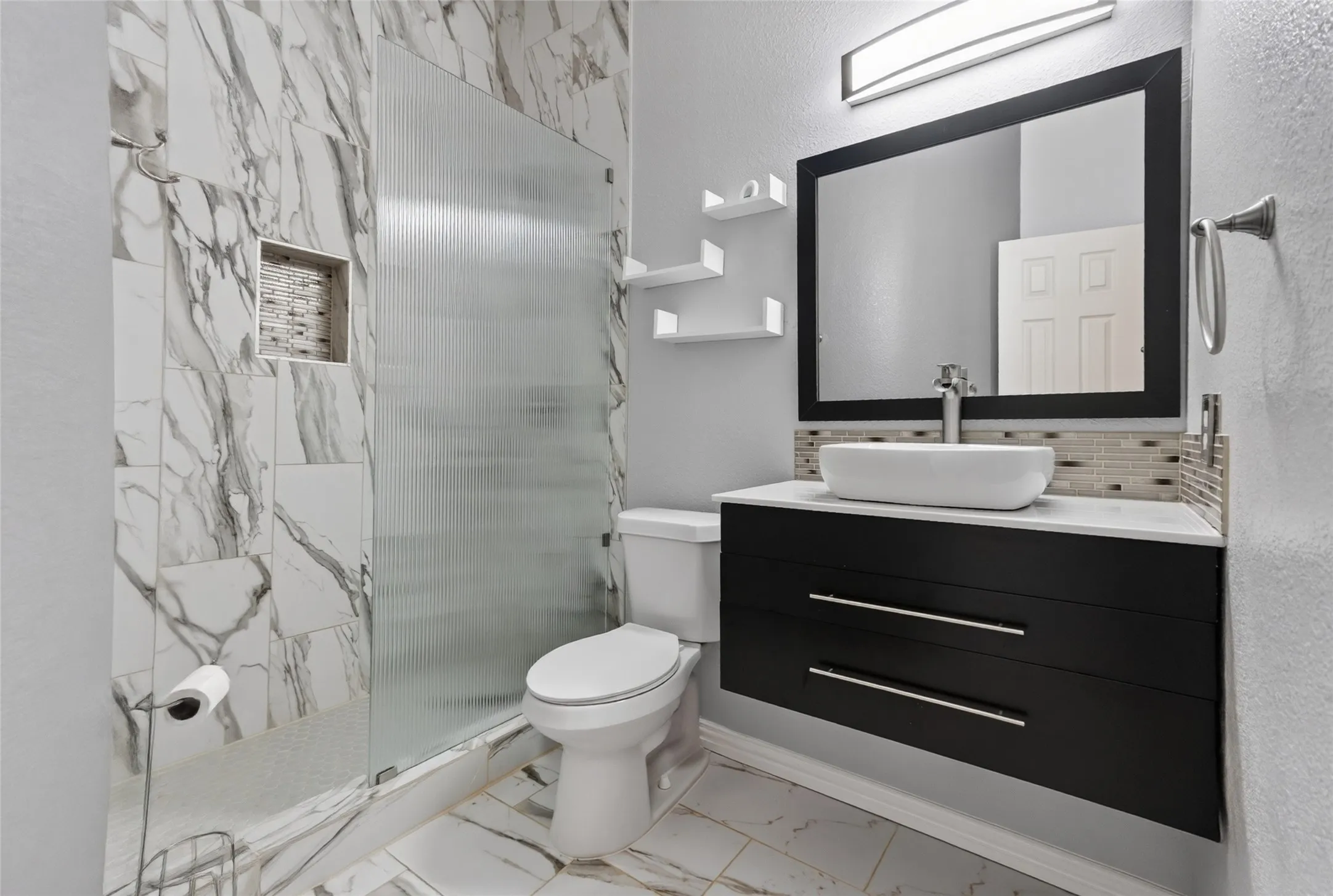 Bathroom featuring a floating vanity with a vessel sink, a full shower with a built-in niche, and large format marble-look tile on the walls and flooring (1st floor)