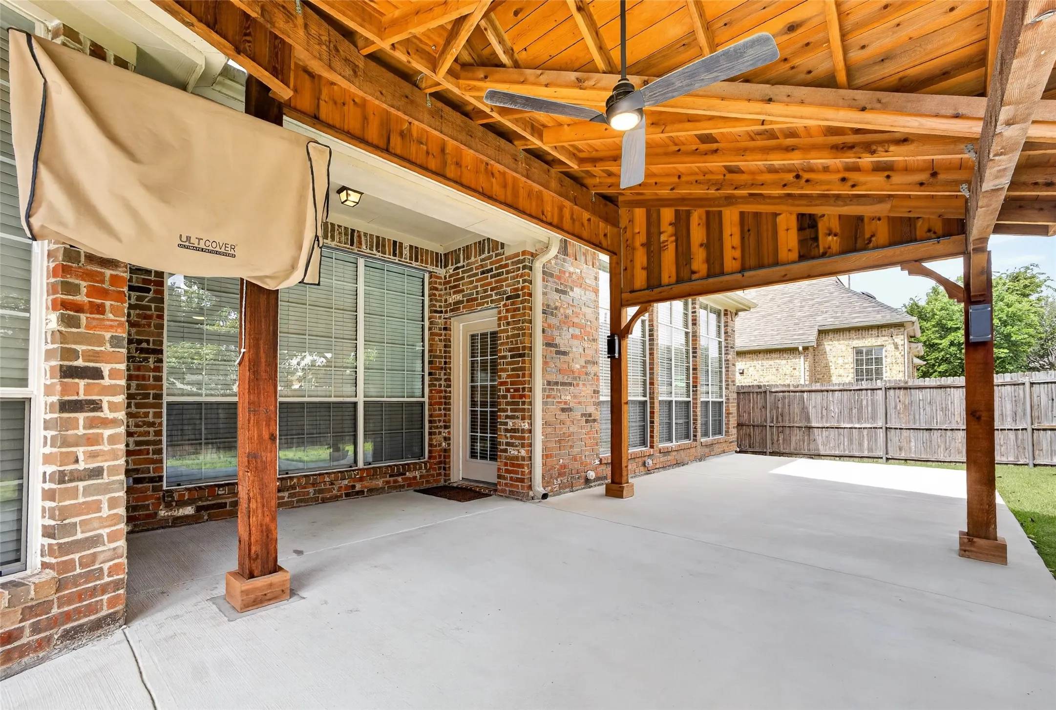 Spacious covered custom patio with lightsfd featuring a natural wood ceiling, exposed beams, and concrete flooring