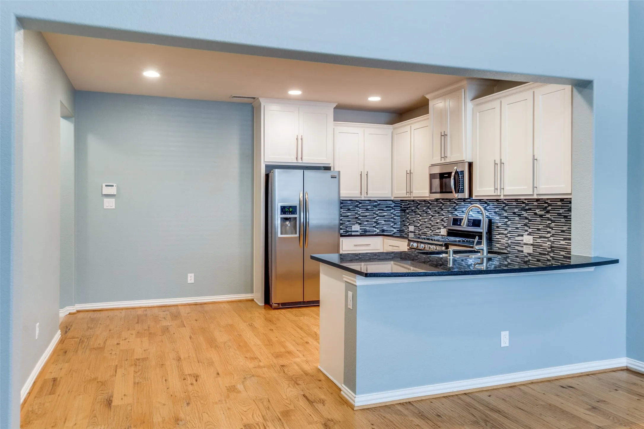 Kitchen with appliances with stainless steel finishes, a sink, light wood-style floors, a peninsula, and tasteful backsplash