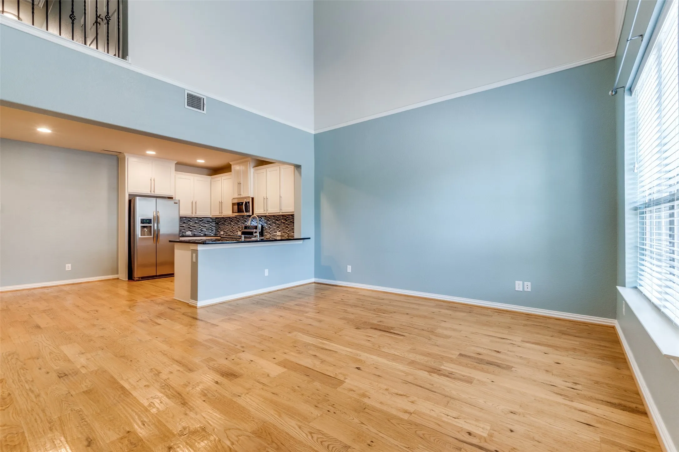 Unfurnished living room with light wood finished floors, plenty of natural light, baseboards, and a high ceiling