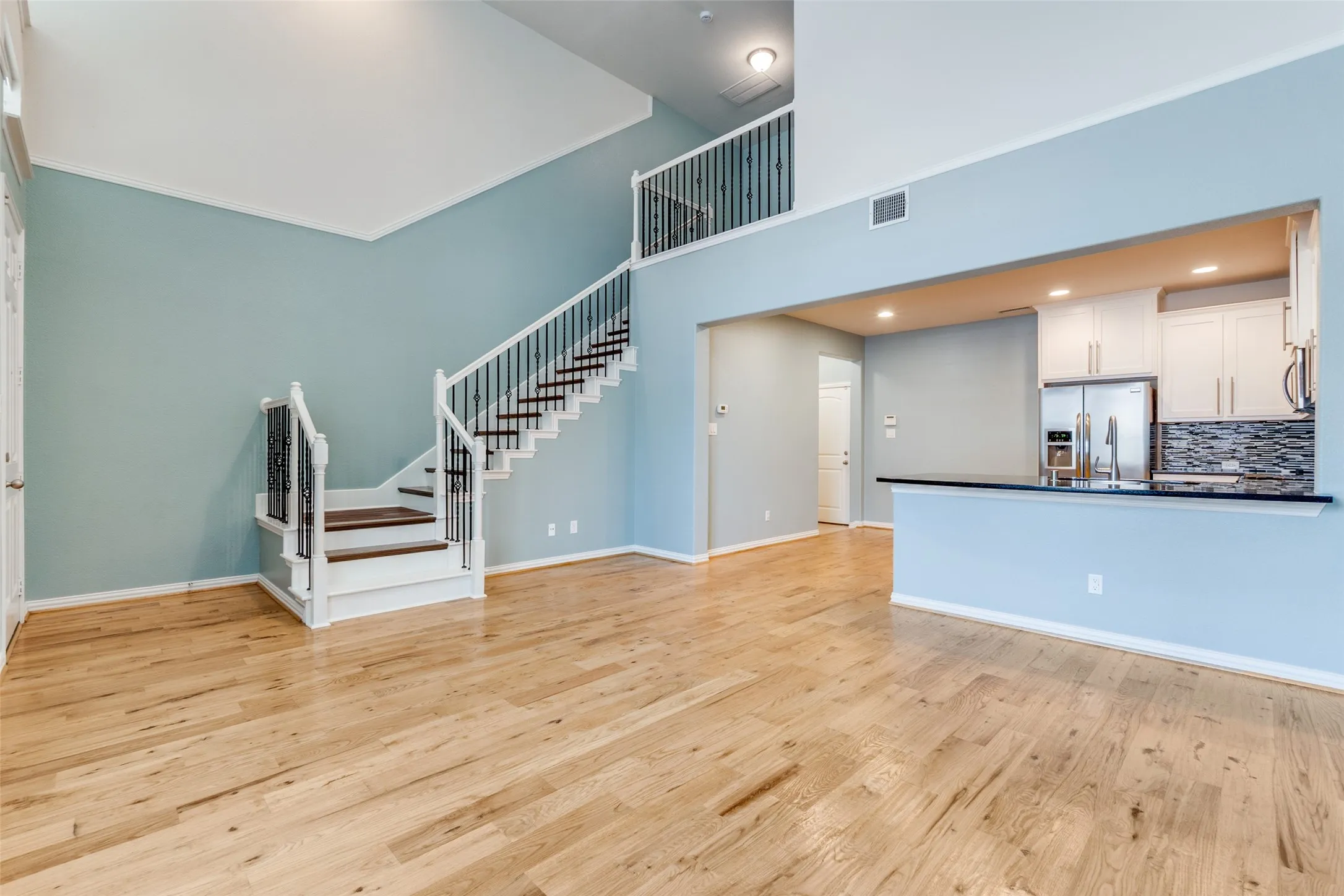 Unfurnished living room featuring stairway, light wood finished floors, baseboards, and a high ceiling