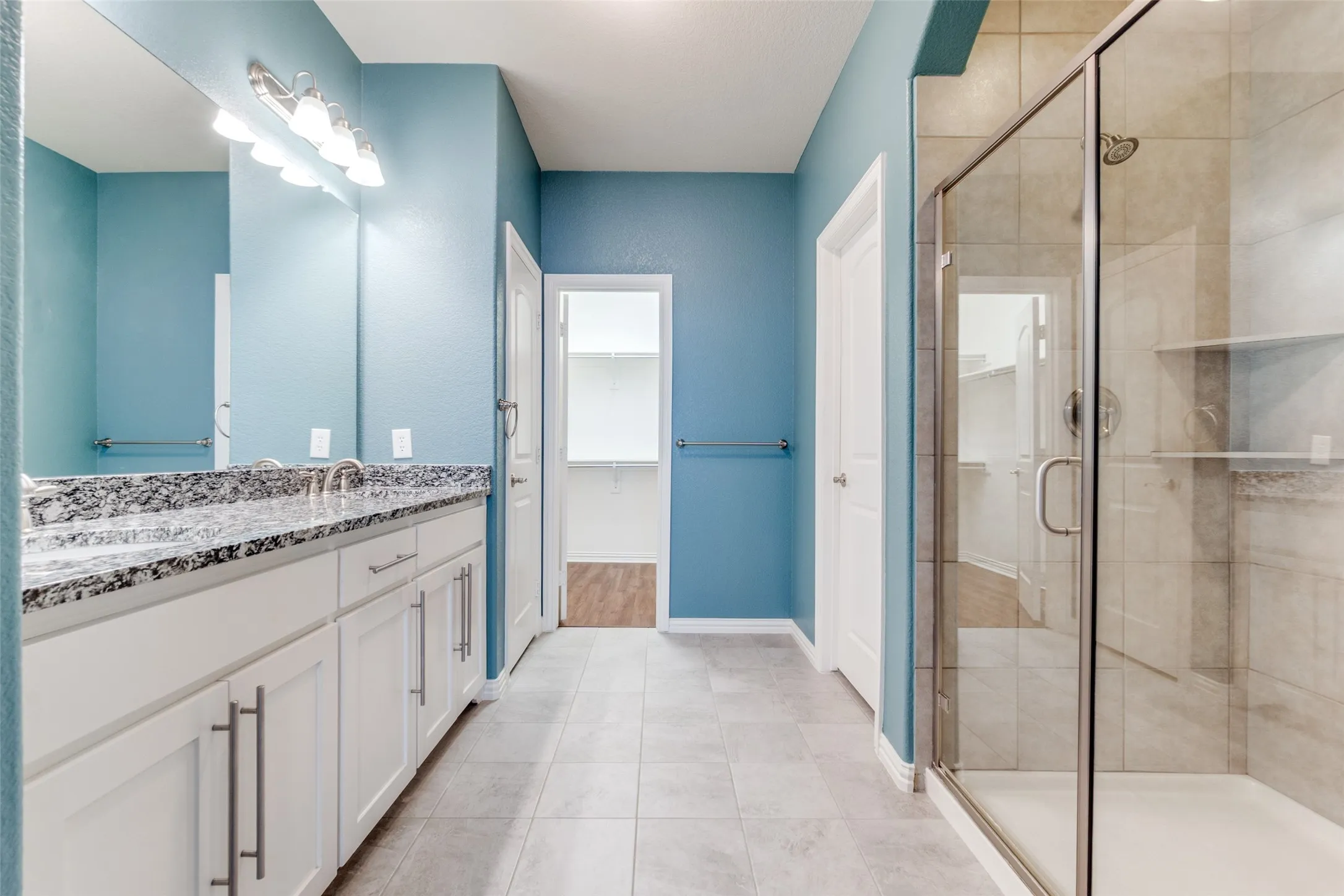 Bathroom with a shower stall, double vanity, baseboards, tile patterned floors, and a walk in closet