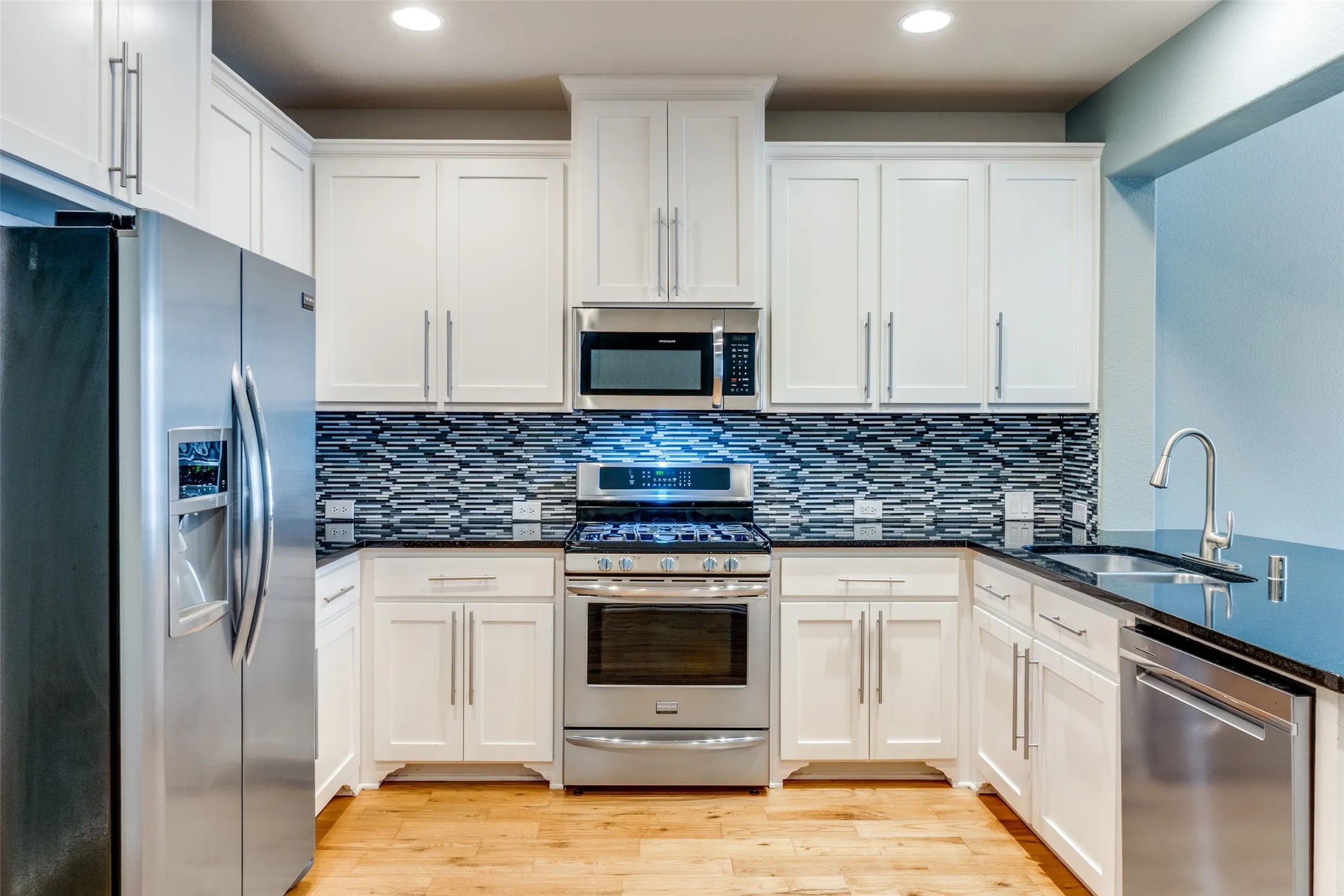 Kitchen featuring stainless steel appliances, a sink, backsplash, white cabinets, and recessed lighting